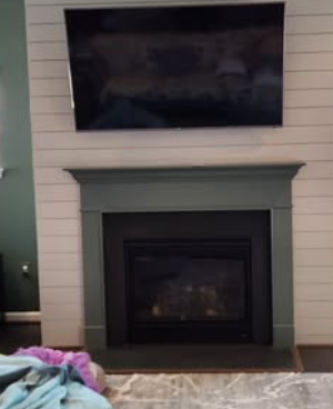 Fireplace with a black hearth, green trim, and a mounted TV on a shiplap wall.