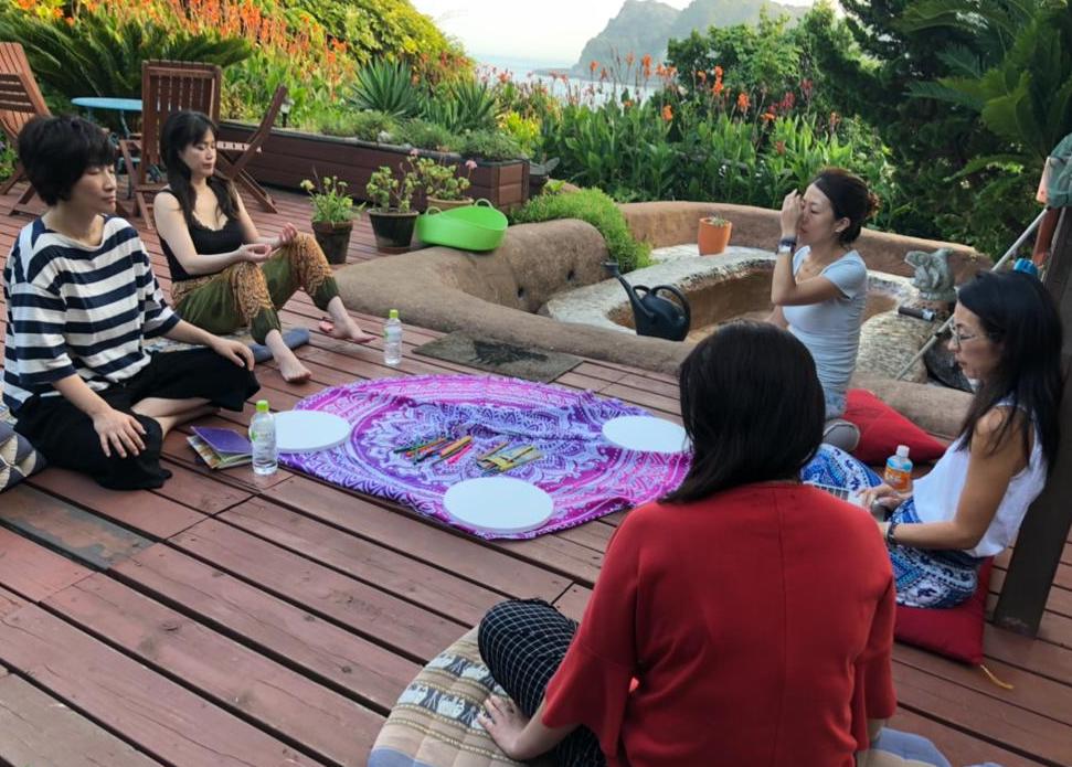 A group of women are sitting in a circle on a wooden deck.