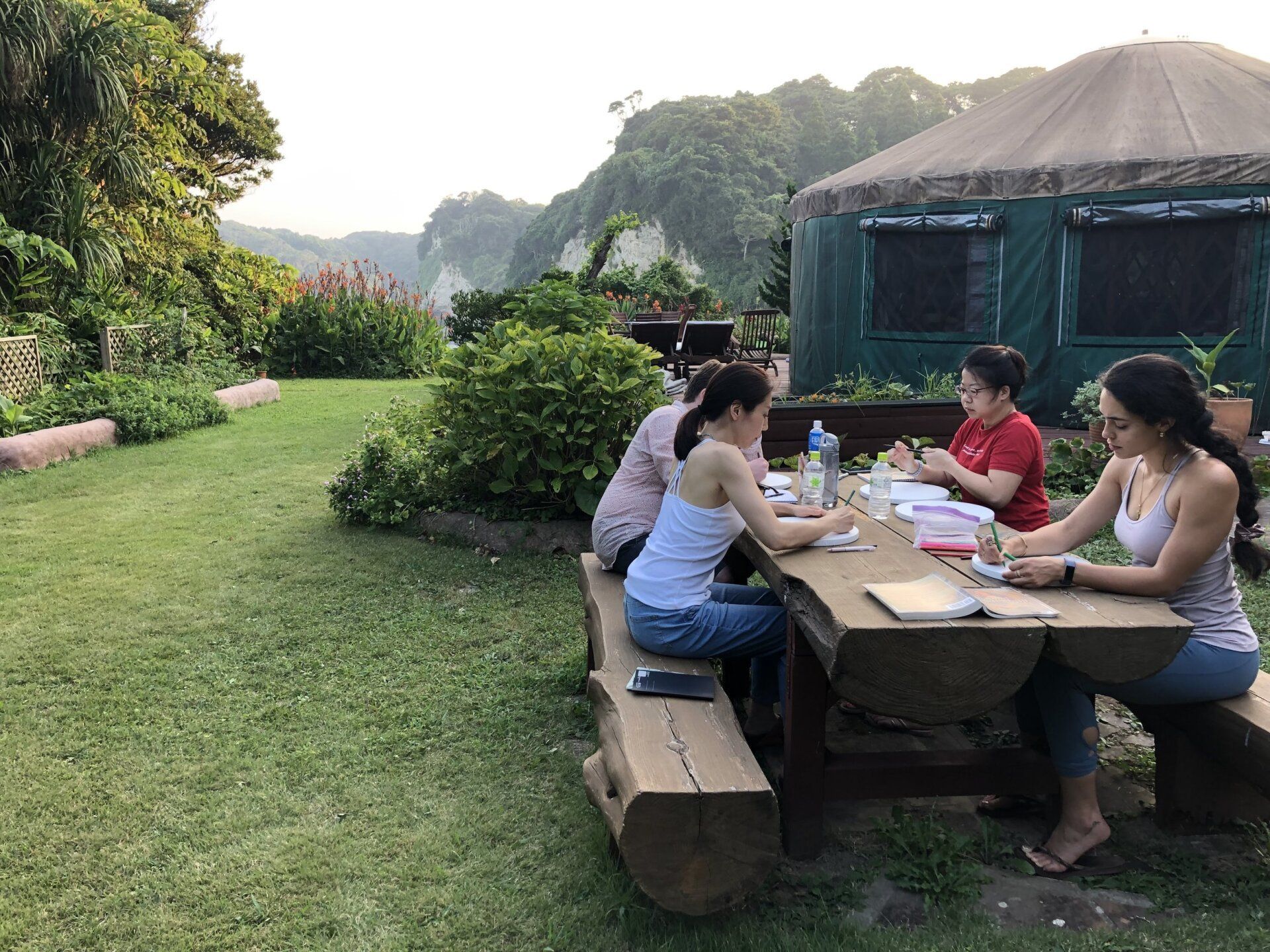 A group of people are sitting at a picnic table in the grass.