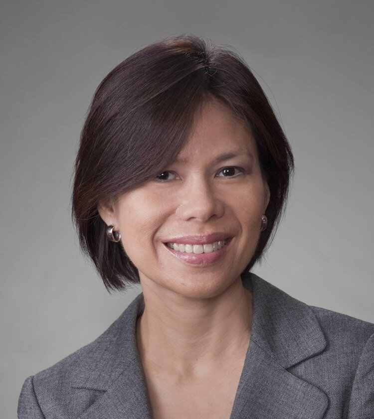 A woman wearing a grey jacket and earrings smiles for the camera