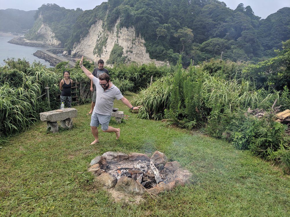 A man is jumping in the air in front of a fire pit.