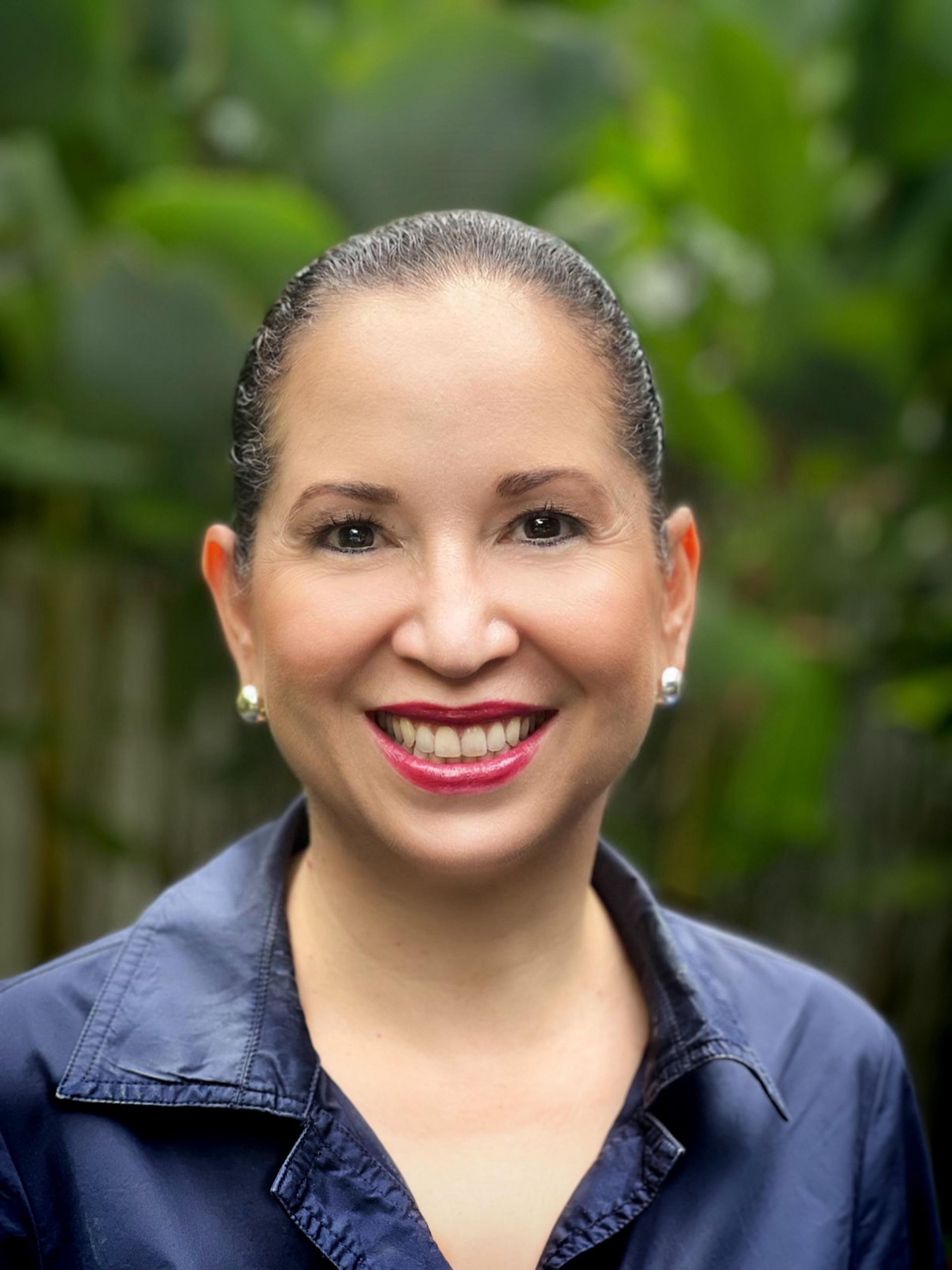 A woman wearing a blue shirt and earrings smiles for the camera