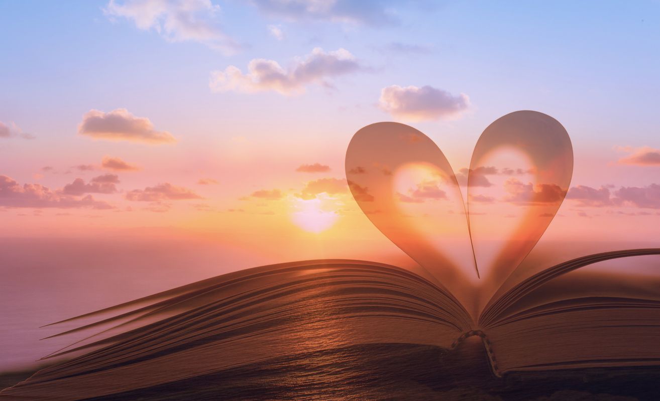 An open book with a heart shaped shadow on the pages at sunset.