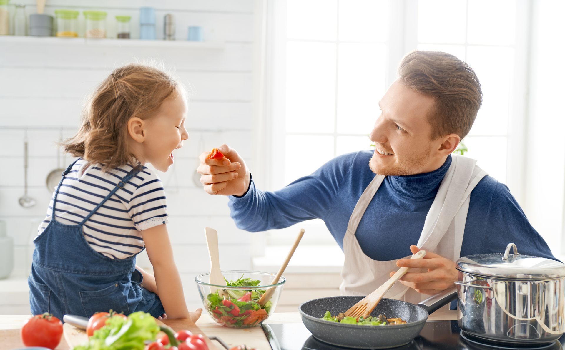 A man and a little girl are cooking together in a kitchen.