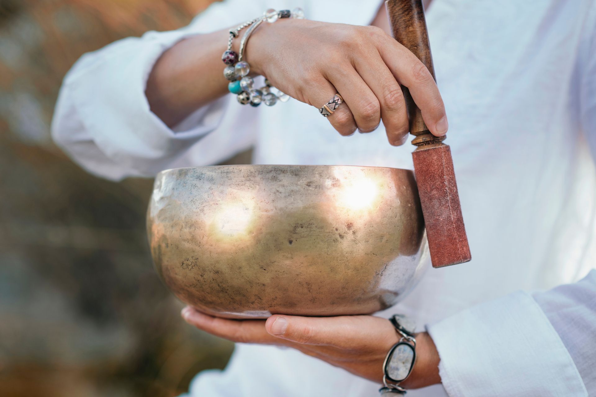 A woman is holding a singing bowl with a wooden stick in her hands.