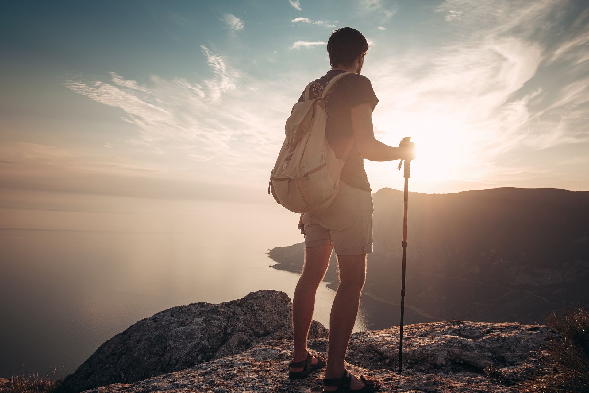 A man with a backpack and hiking poles is standing on top of a mountain.