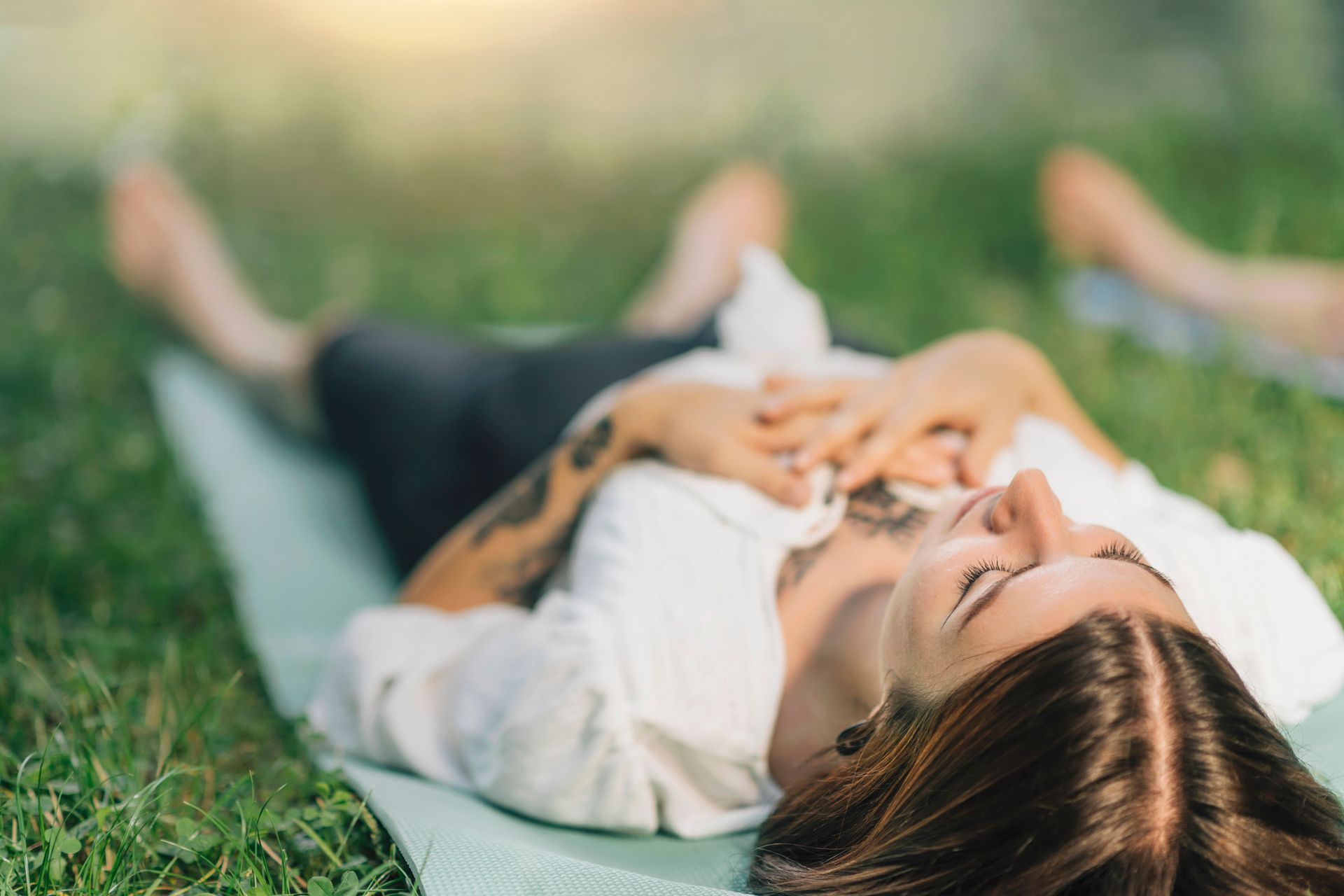 A woman is laying on a yoga mat in the grass.