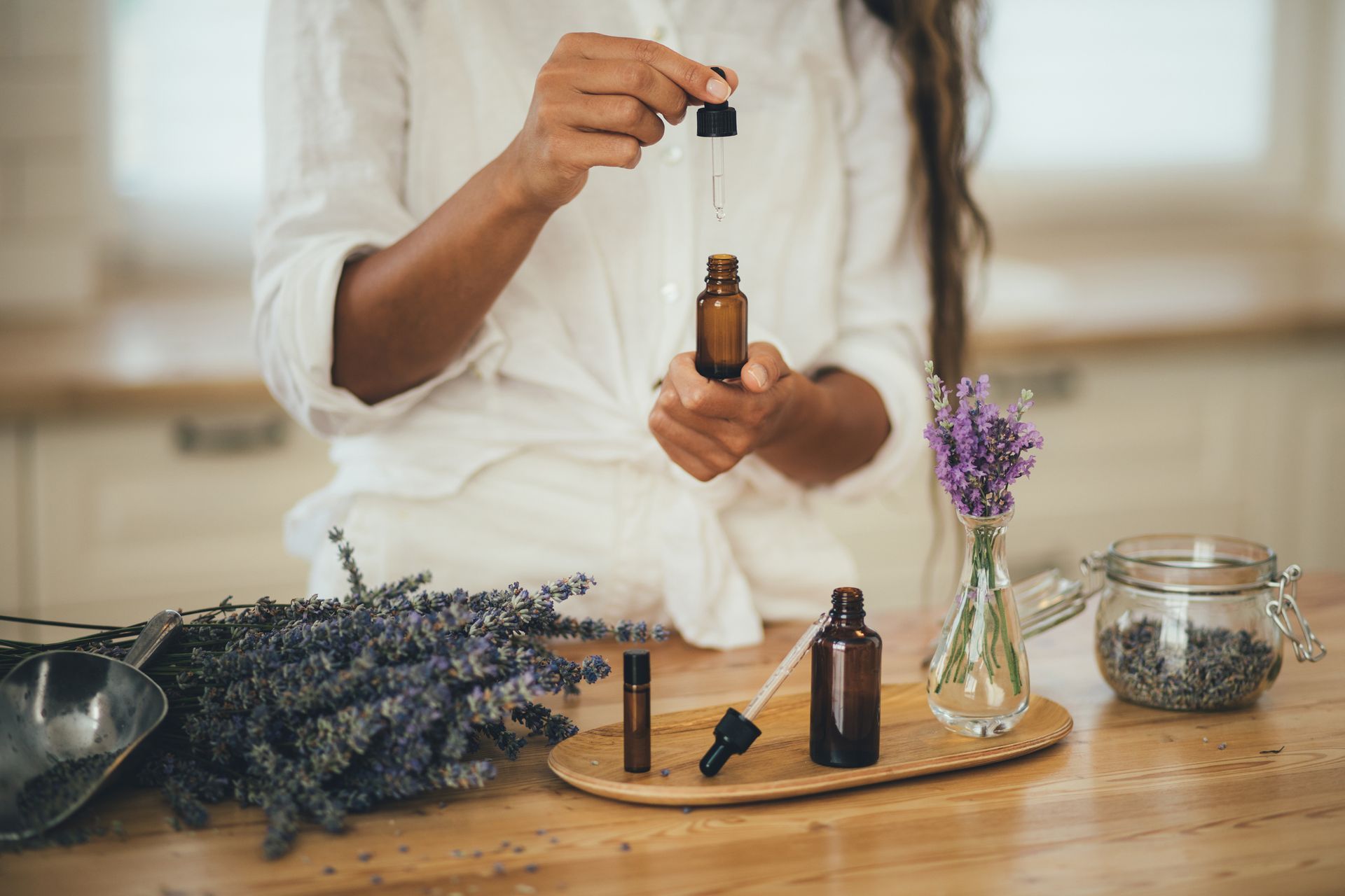 A woman is pouring essential oil into a bottle with a pipette.