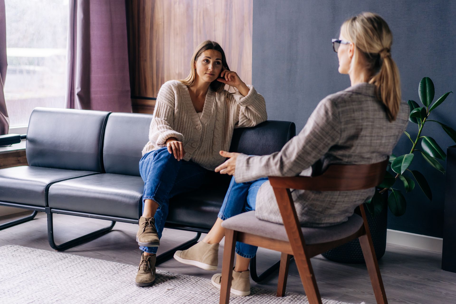 Two women are sitting on a couch talking to each other.