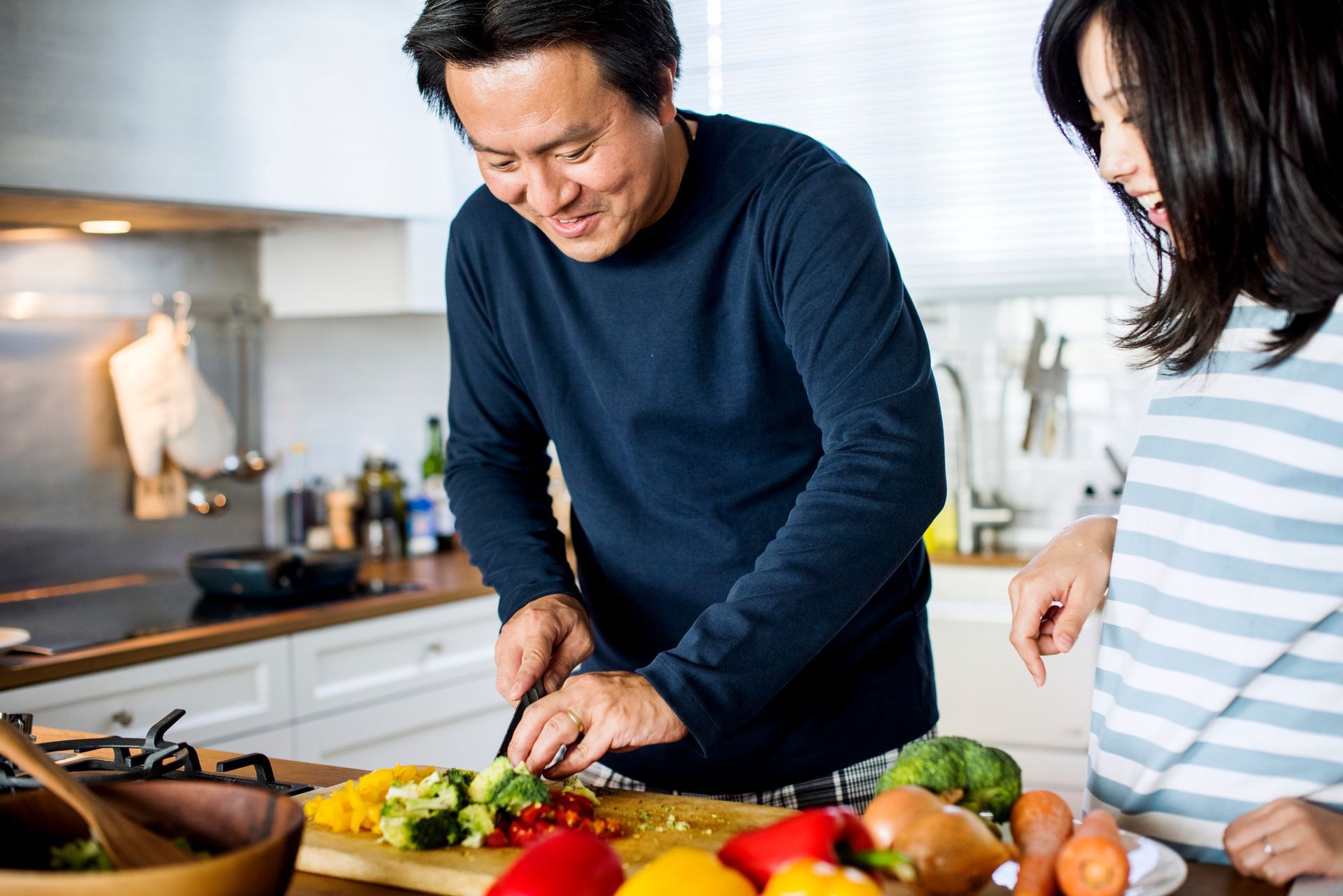 A man and a woman are cutting vegetables on a cutting board in a kitchen.