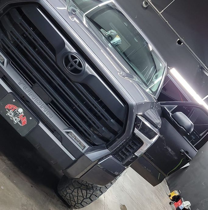 Black Toyota pickup truck in a garage, angled view with front grille and open driver door.