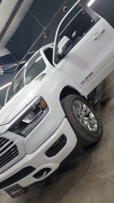 White pickup truck displayed indoors on a showroom floor, angled view with chrome wheels and grille.
