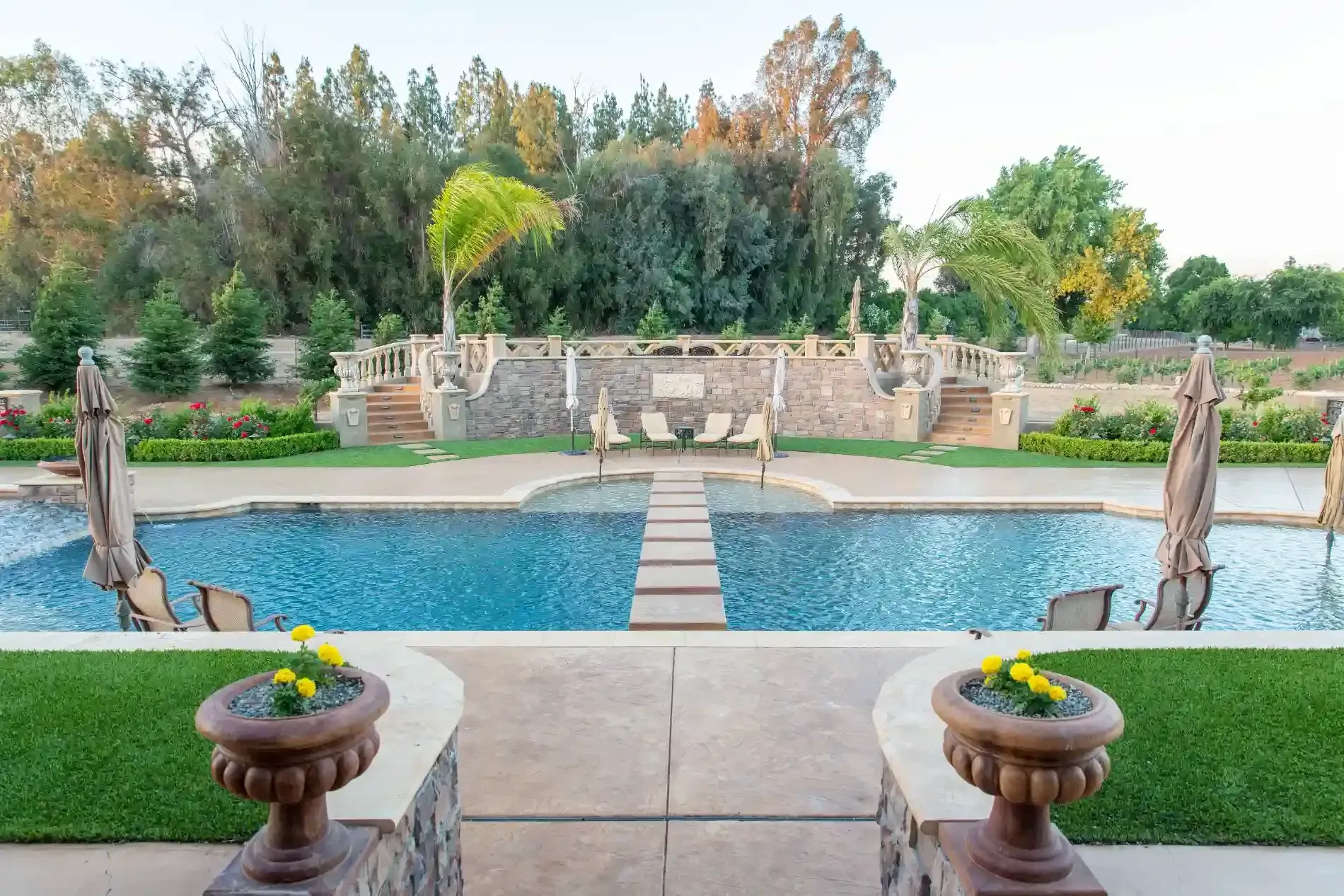 Backyard pool with stone patio, potted flowers, and a landscaped garden wall beyond