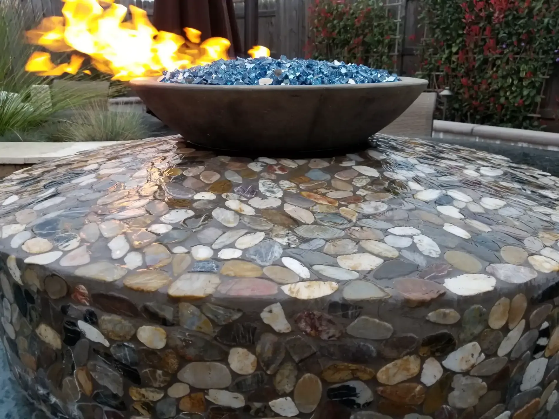 Outdoor stone fire bowl with blue glass fire feature and flames on a mosaic stone patio