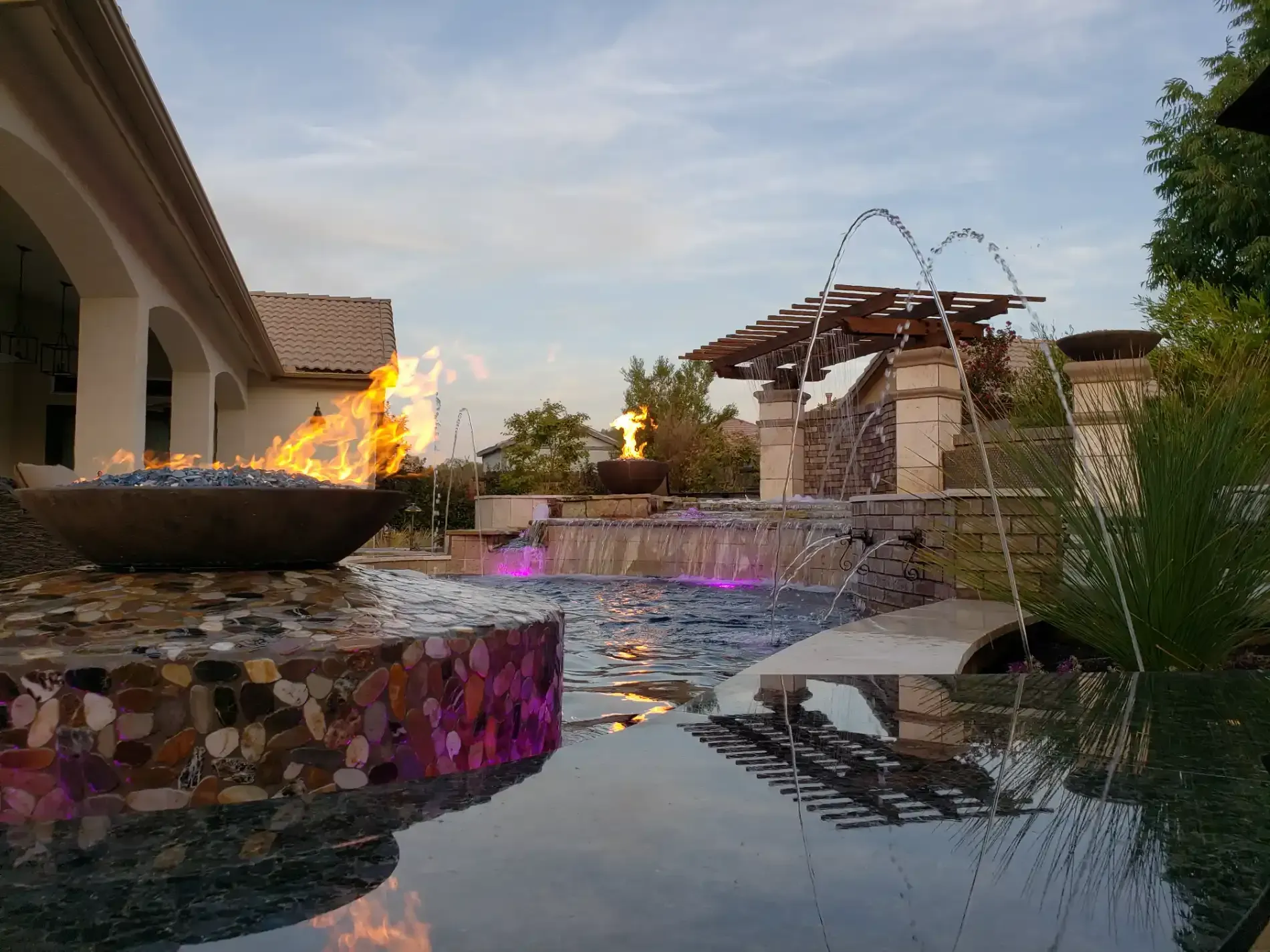 Outdoor pool with fire bowls, water fountains, and a sunset view beside a patio