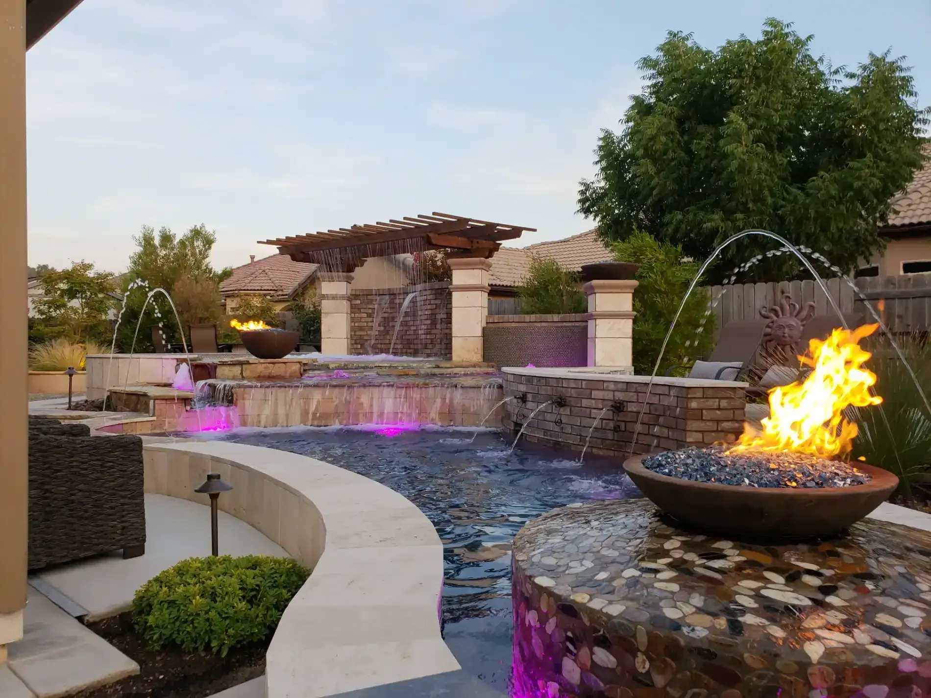 Courtyard water feature with curved pool, glowing fire bowl, and purple-lit fountain at dusk