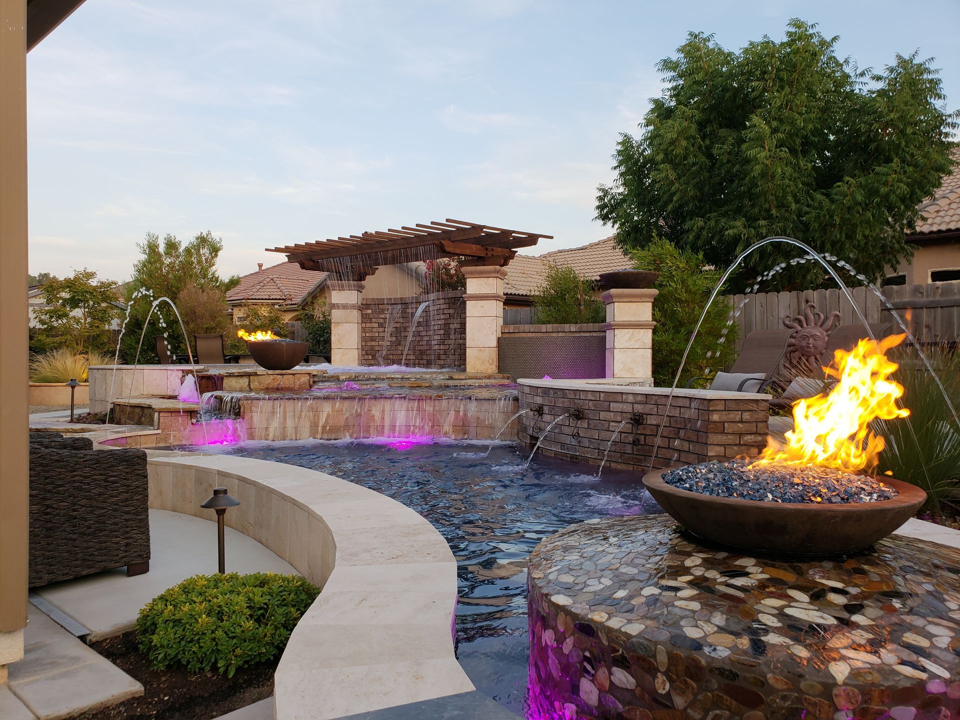 Backyard pool with stone waterfall, purple lights, and a fire bowl beside a curved patio