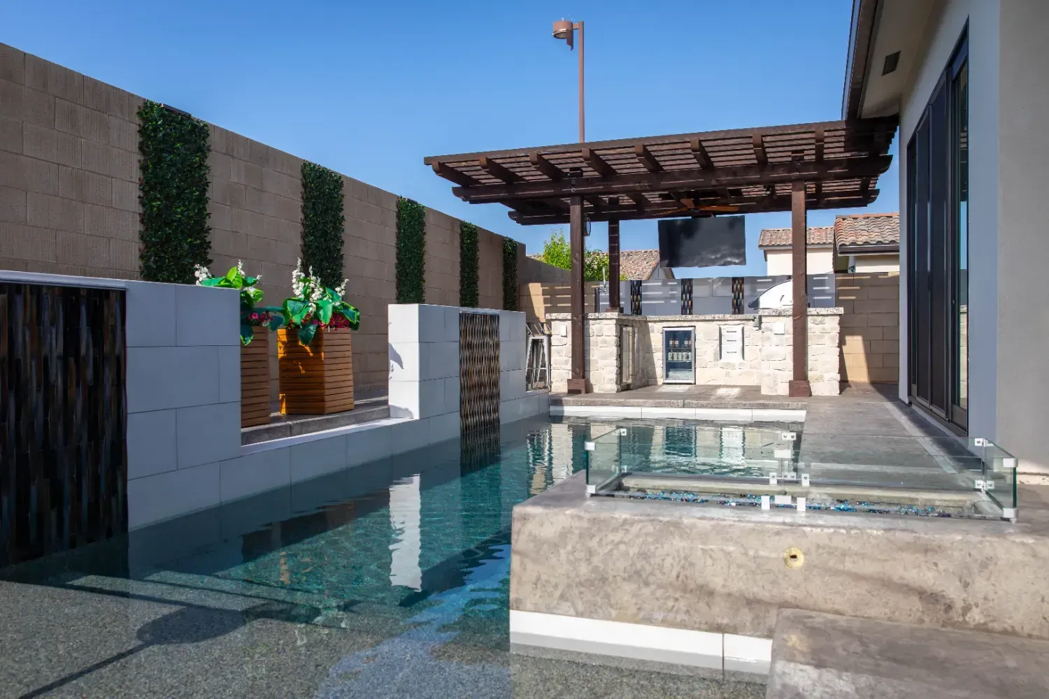 Modern backyard pool with pergola, glass railing, and white walls under a clear blue sky