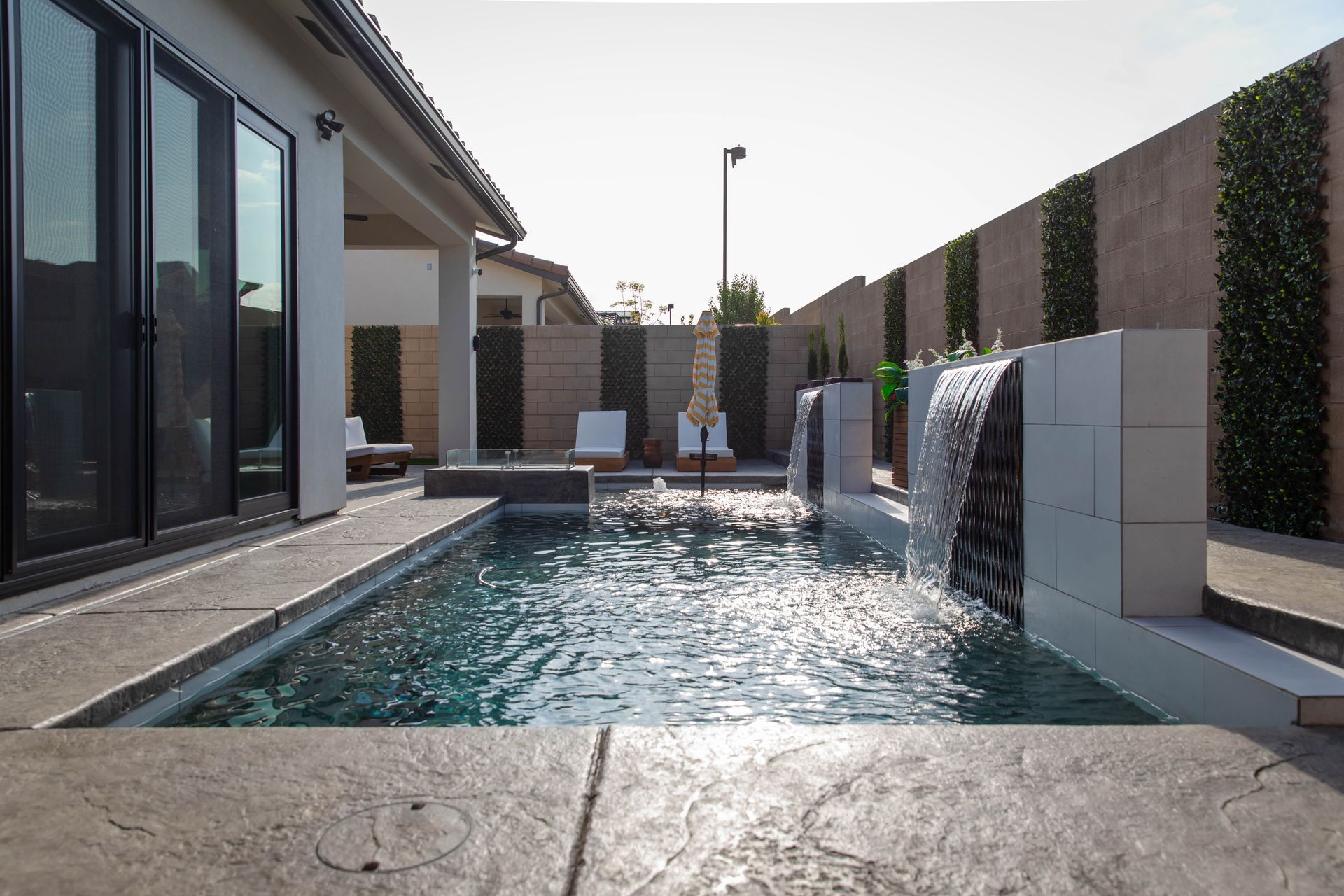 Backyard pool with water features beside a modern house on a sunny day