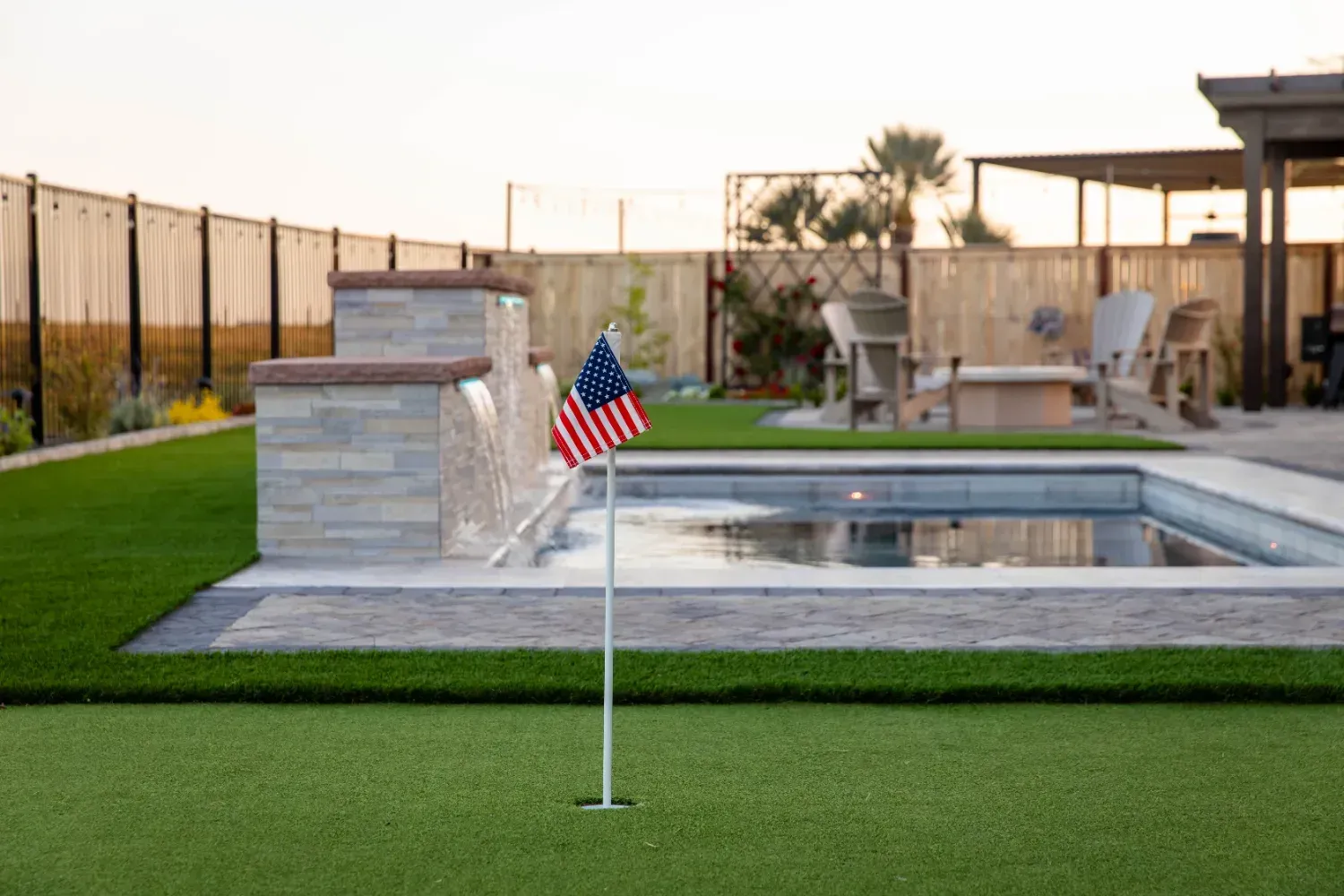 Backyard pool with patio, American flag, and grass lawn at sunset
