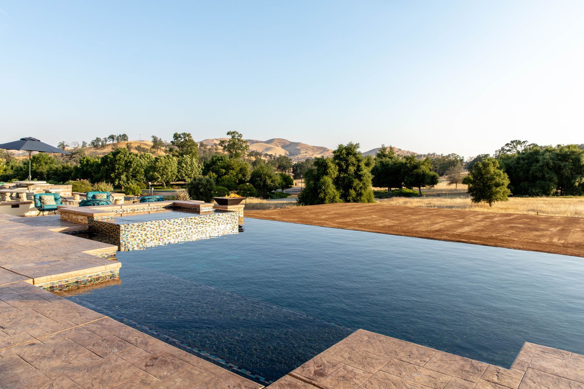 Large blue reflecting pool beside dry fields and trees under a clear sky