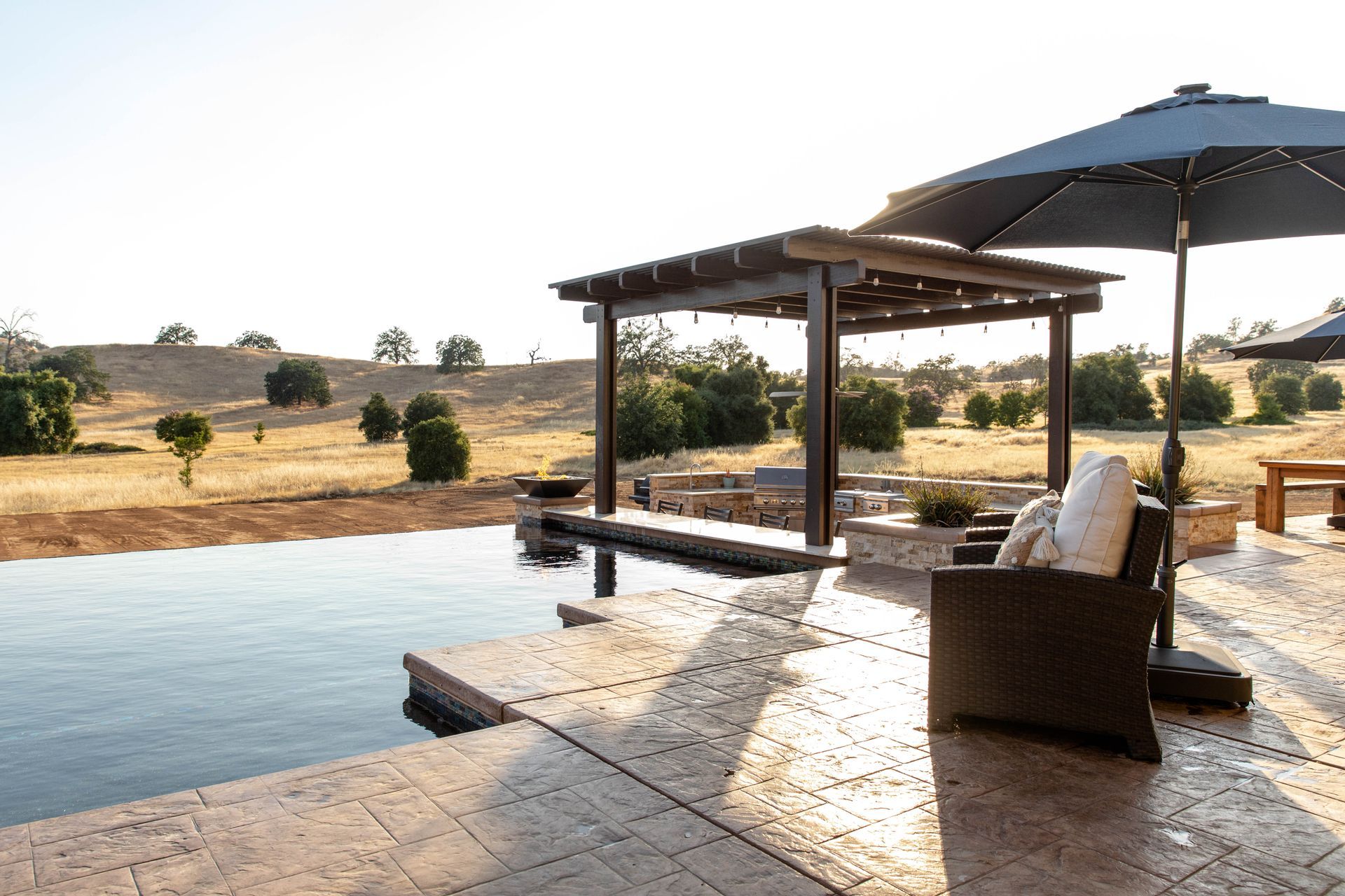 Poolside patio with lounge chair and umbrella overlooking a dry, grassy landscape