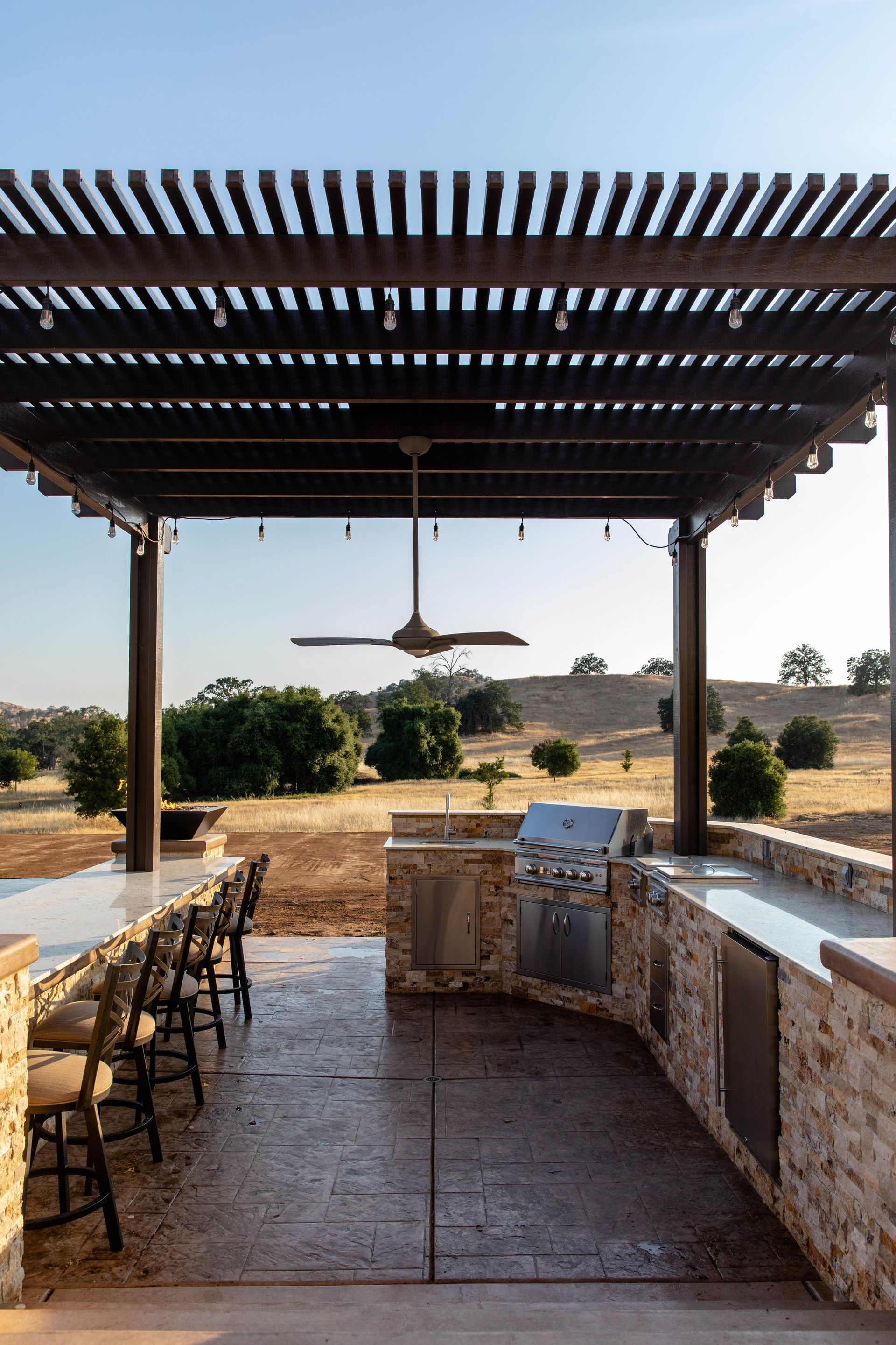 Outdoor pergola dining area with a long table, chairs, and a desert landscape beyond