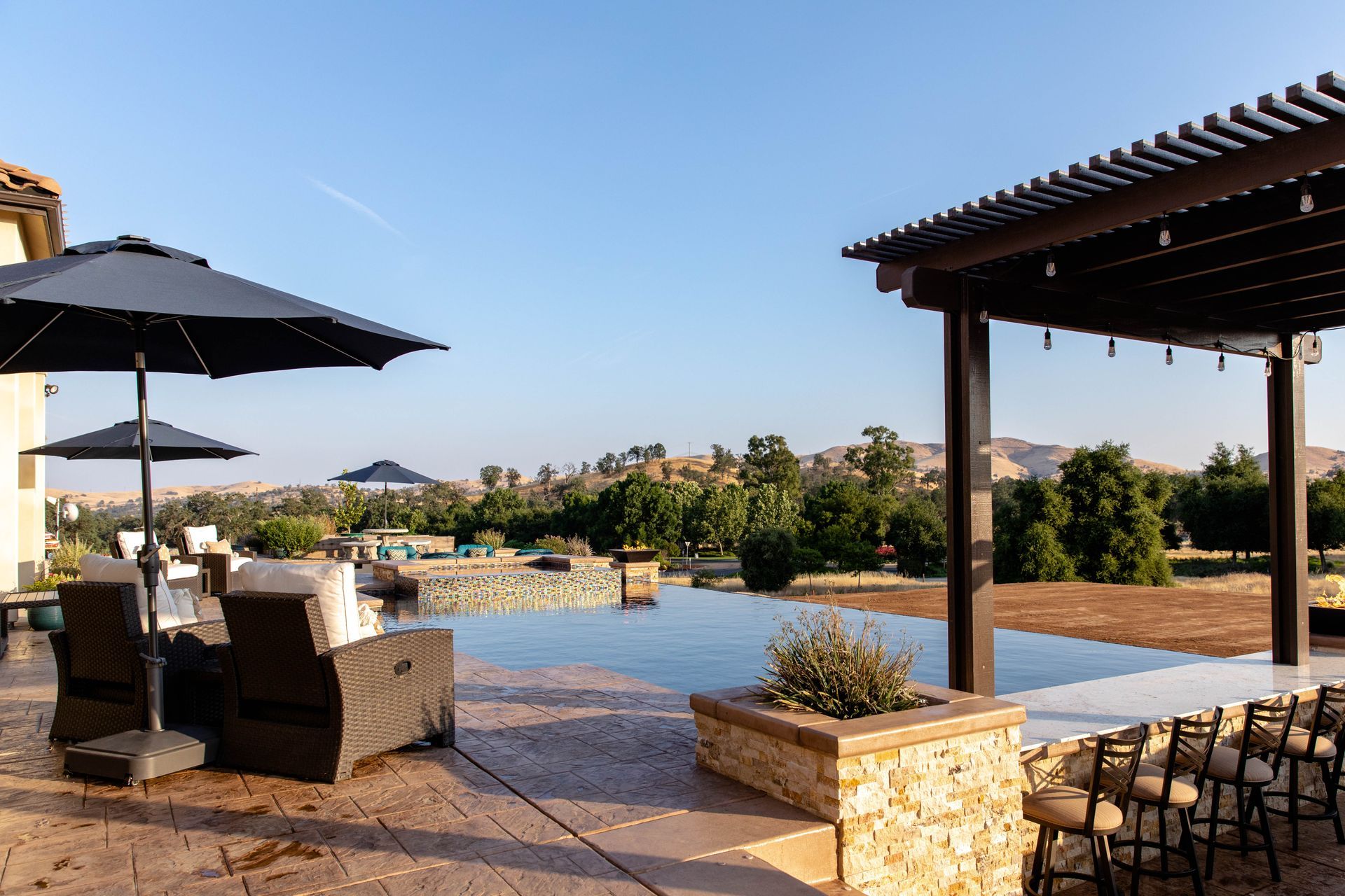 Outdoor patio with lounge chairs, umbrellas, and a poolside view at sunset