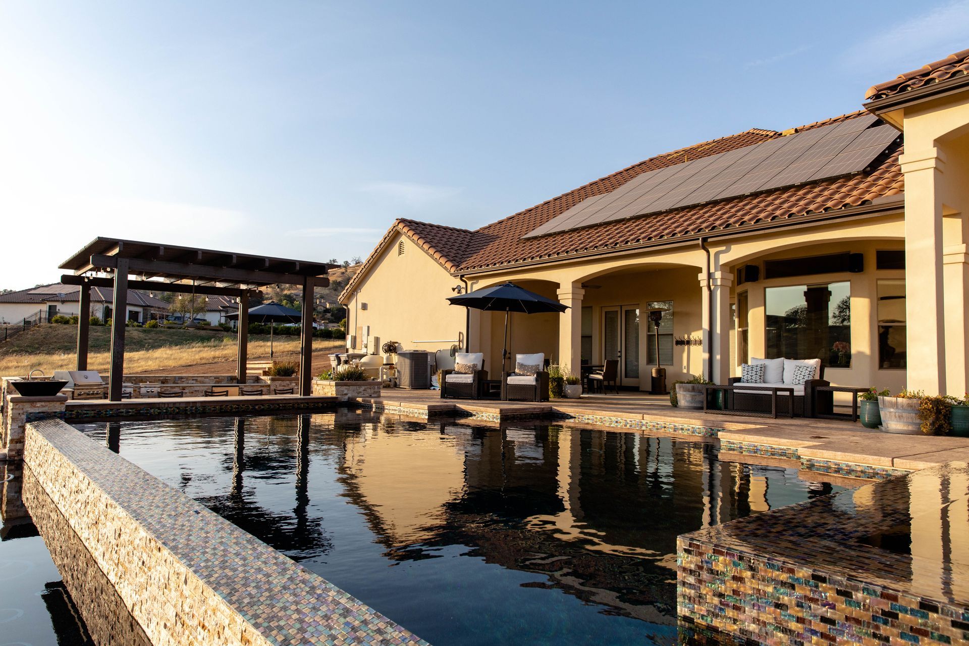 Patio with reflecting pool, covered seating, and tan stucco villa under a clear sky
