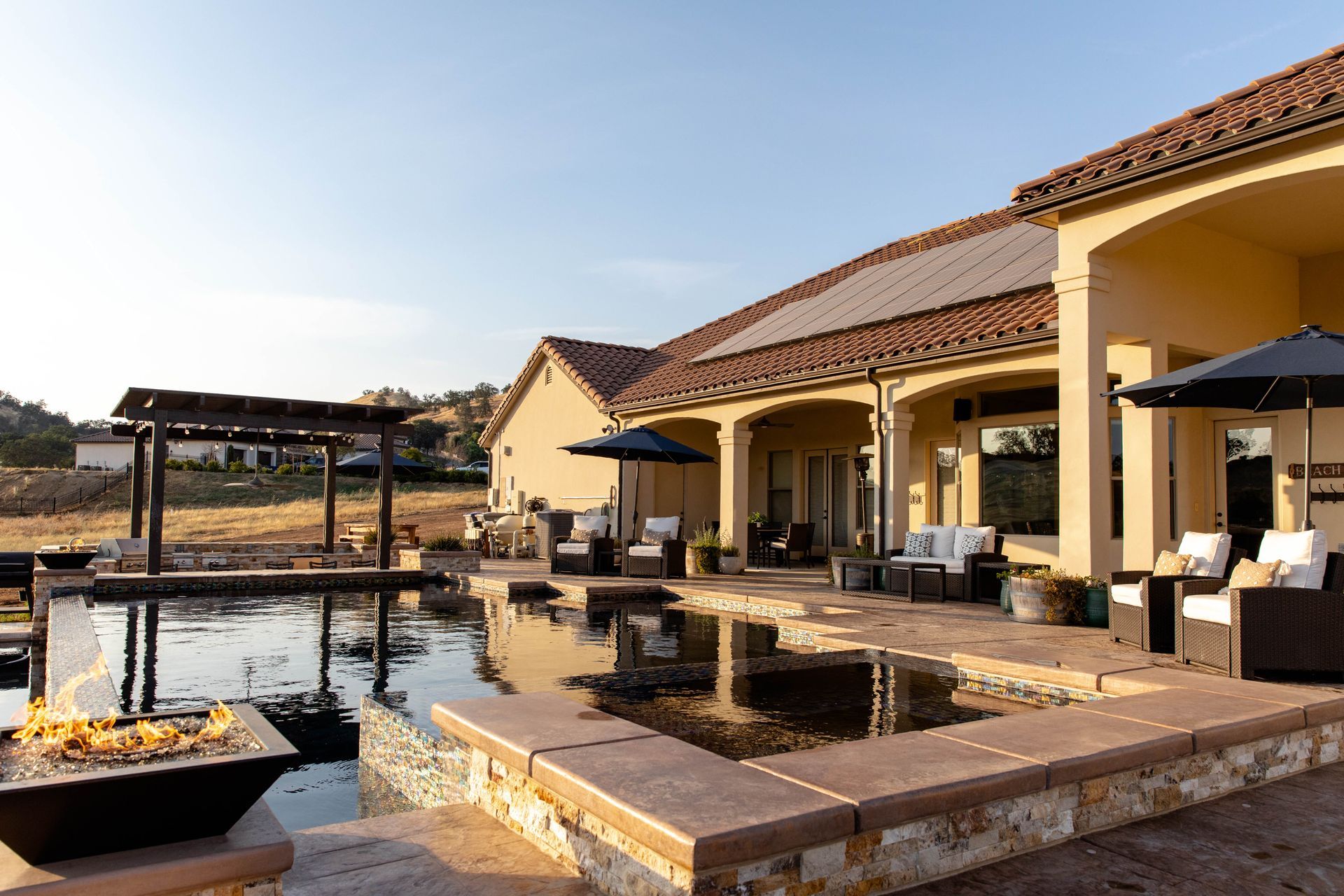 Luxury resort patio with pool, lounge chairs, and umbrellas beside a water feature at sunset