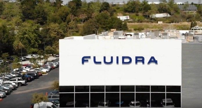 FLUIDRA logo on a white building, with parking lot and trees in the background.