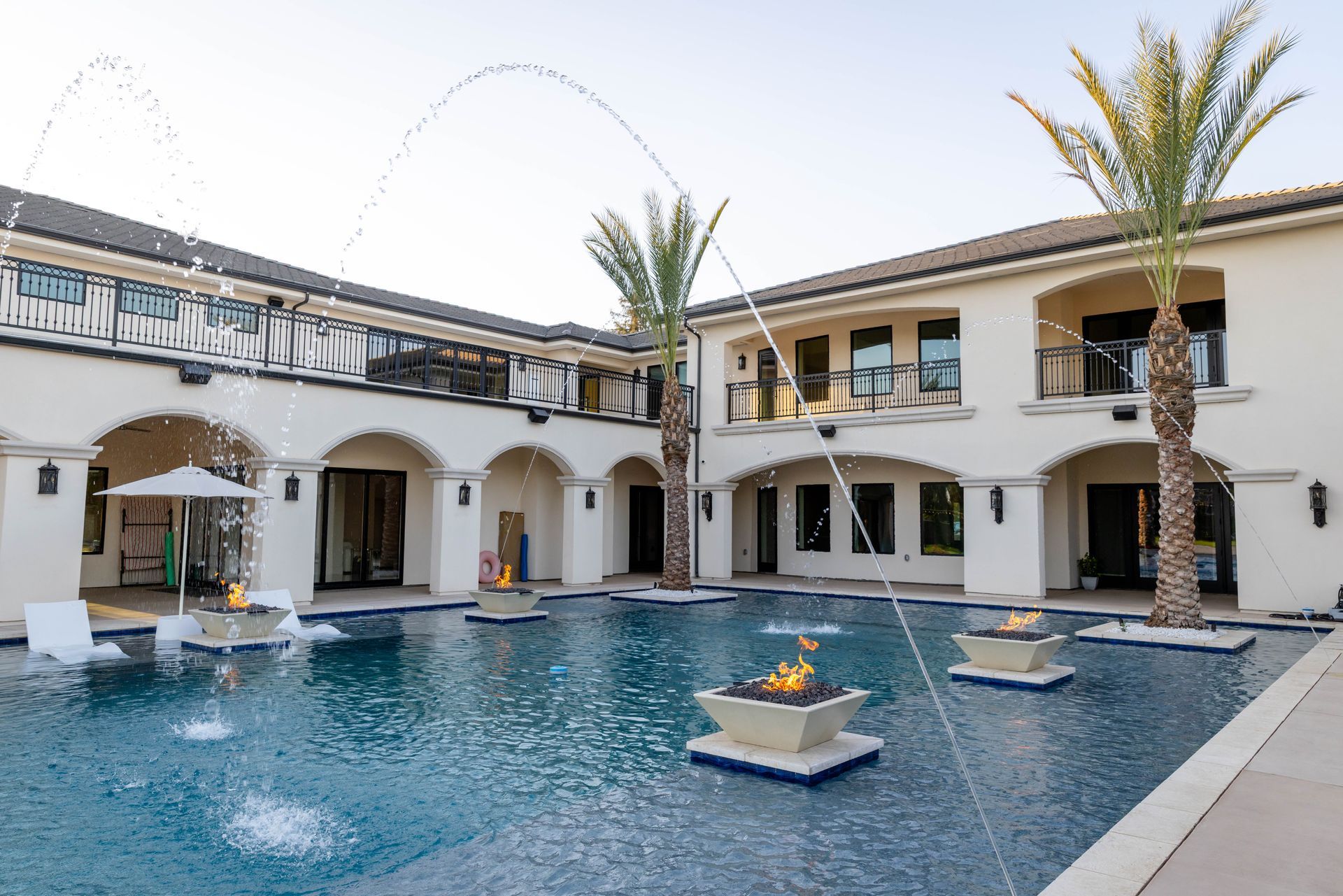 Luxury villa courtyard with a blue swimming pool, arched balconies, and palm trees at dusk