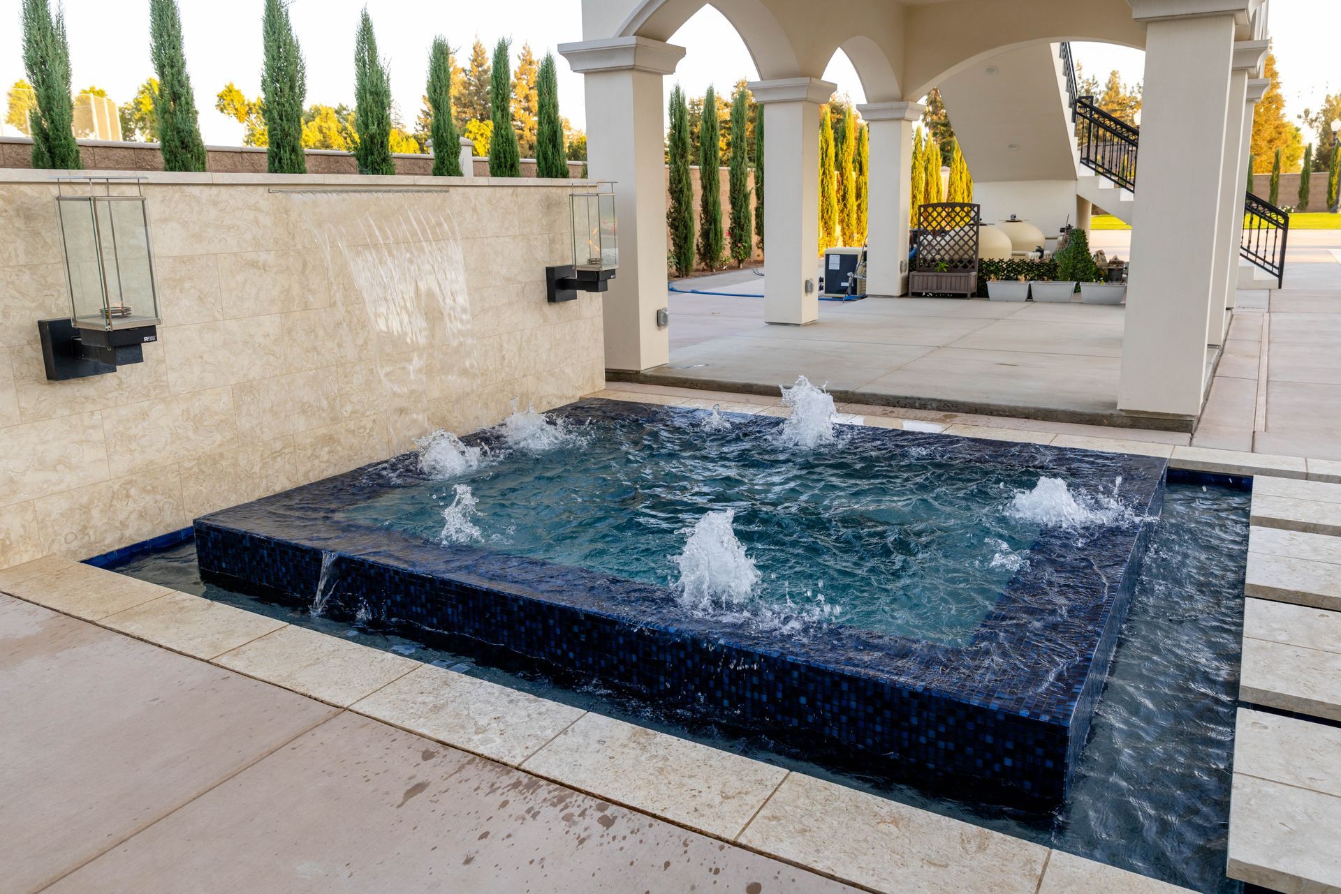Rectangular black fountain pool with water jets beside a stone patio and white arched pavilion