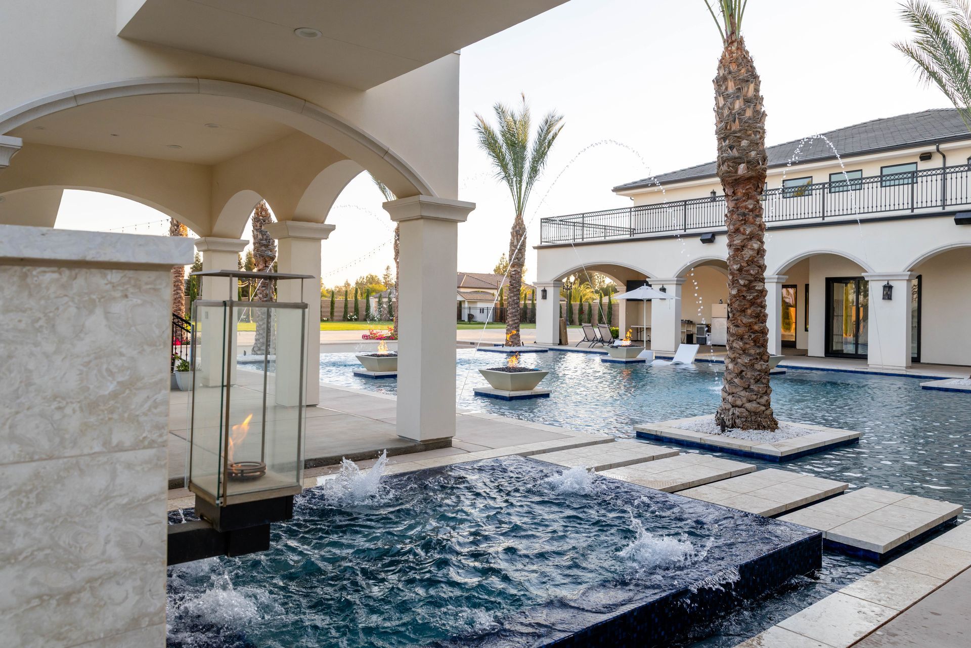 Modern resort courtyard with a shallow pool, palm trees, and arched stone walkways