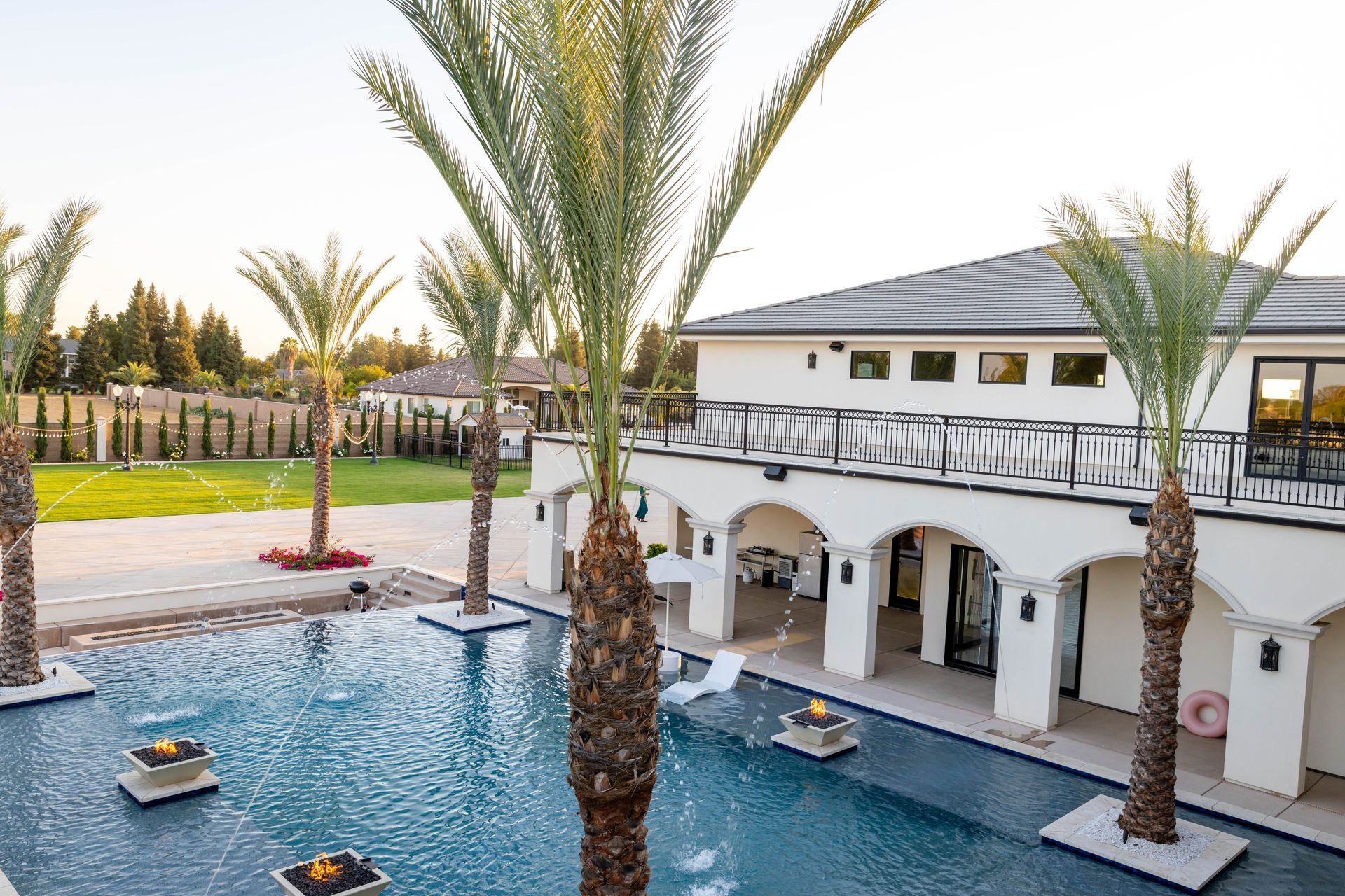 Palm-lined resort pool beside a white villa with lounge chairs and a landscaped courtyard