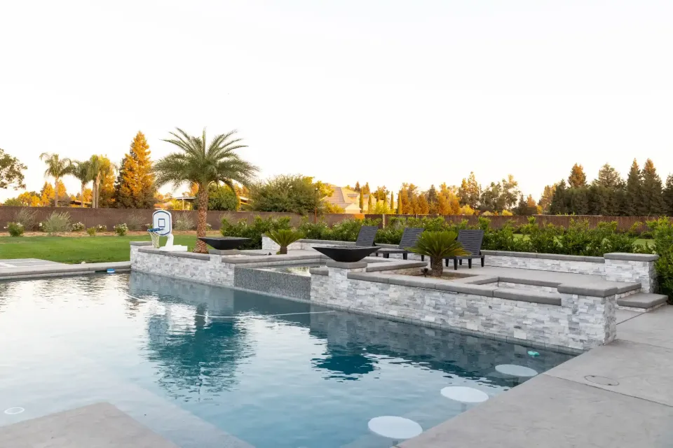 Backyard pool with stone patio, lounge chairs, and palm trees at sunset