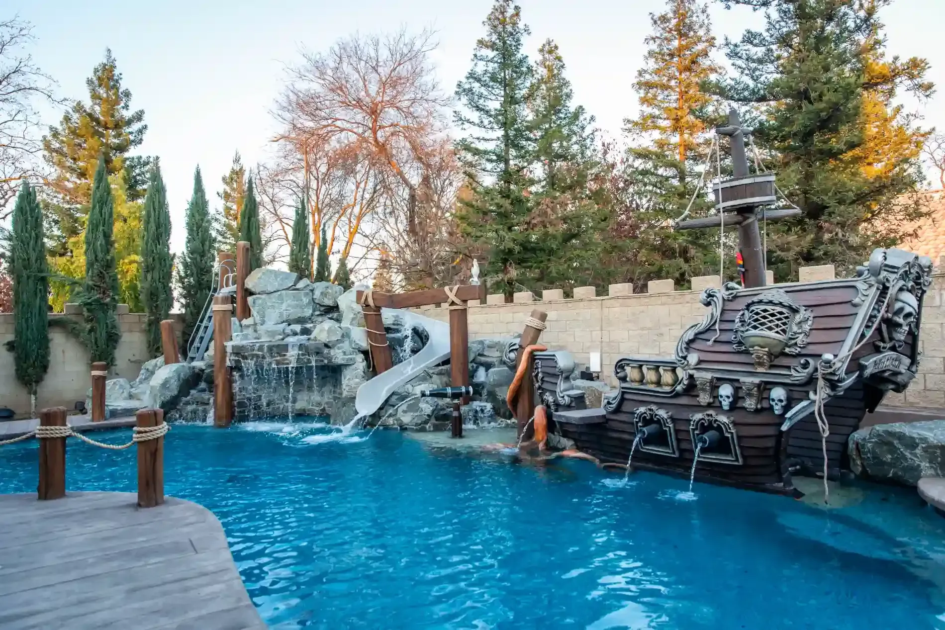 Backyard pool with pirate ship water feature, rock waterfall, and trees in the background