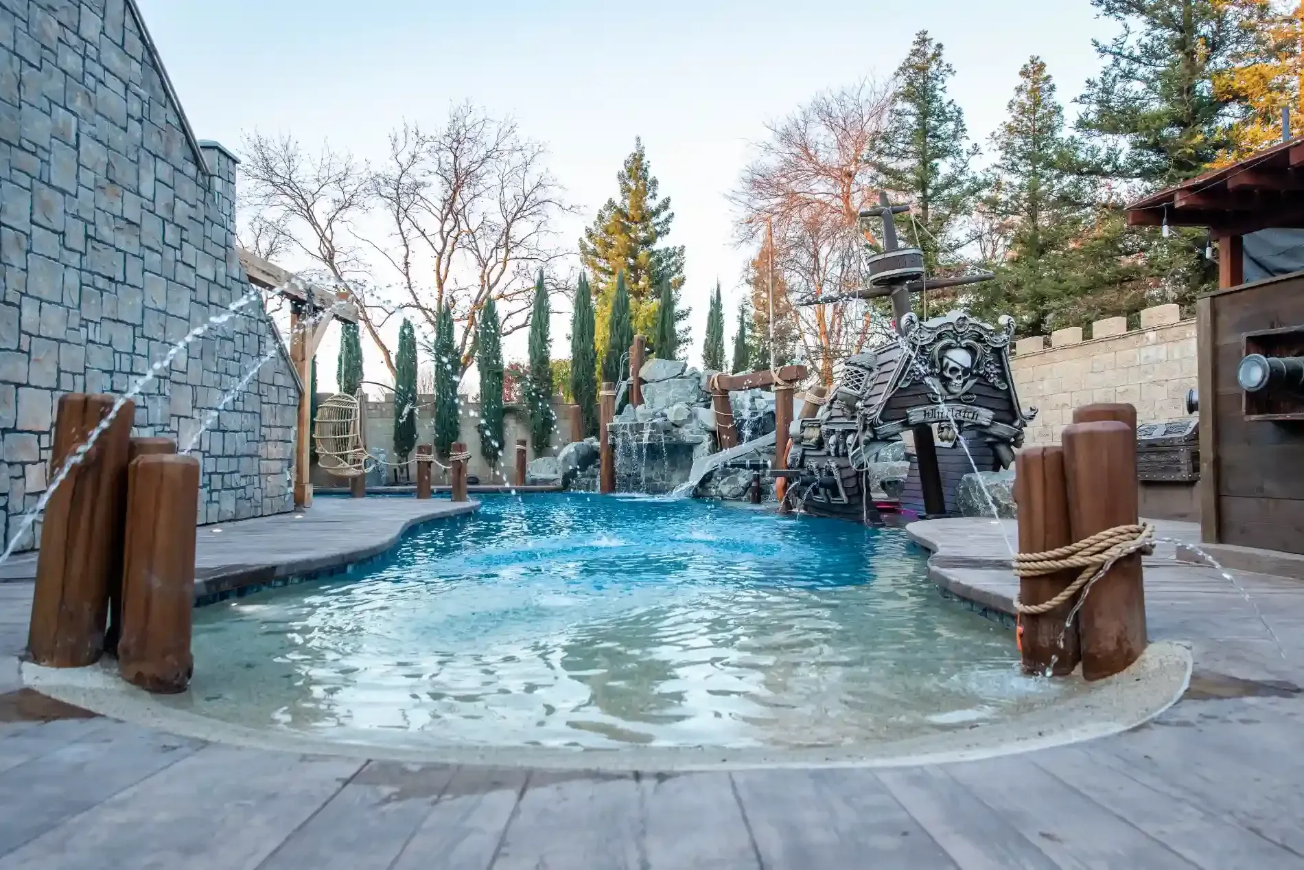 Outdoor stone spa with blue water, surrounded by trees and stone walls