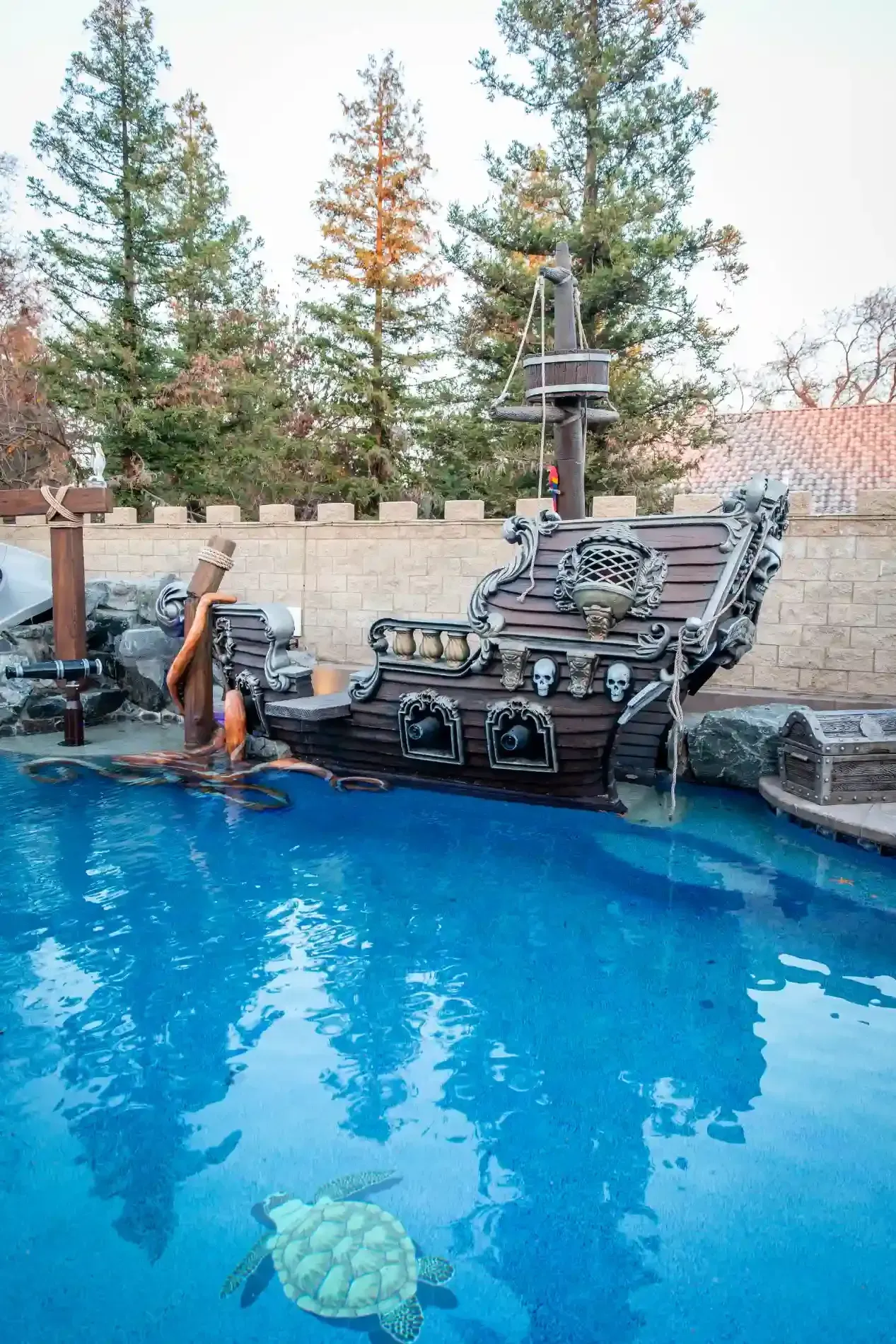 Backyard pool with a chair by the water, stone wall, and trees in the background