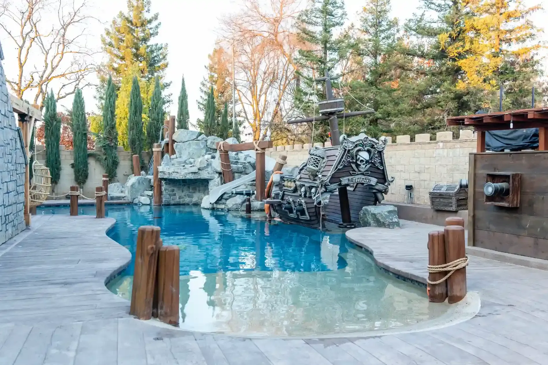 Backyard pool with waterfall, stone deck, and trees in a landscaped outdoor setting