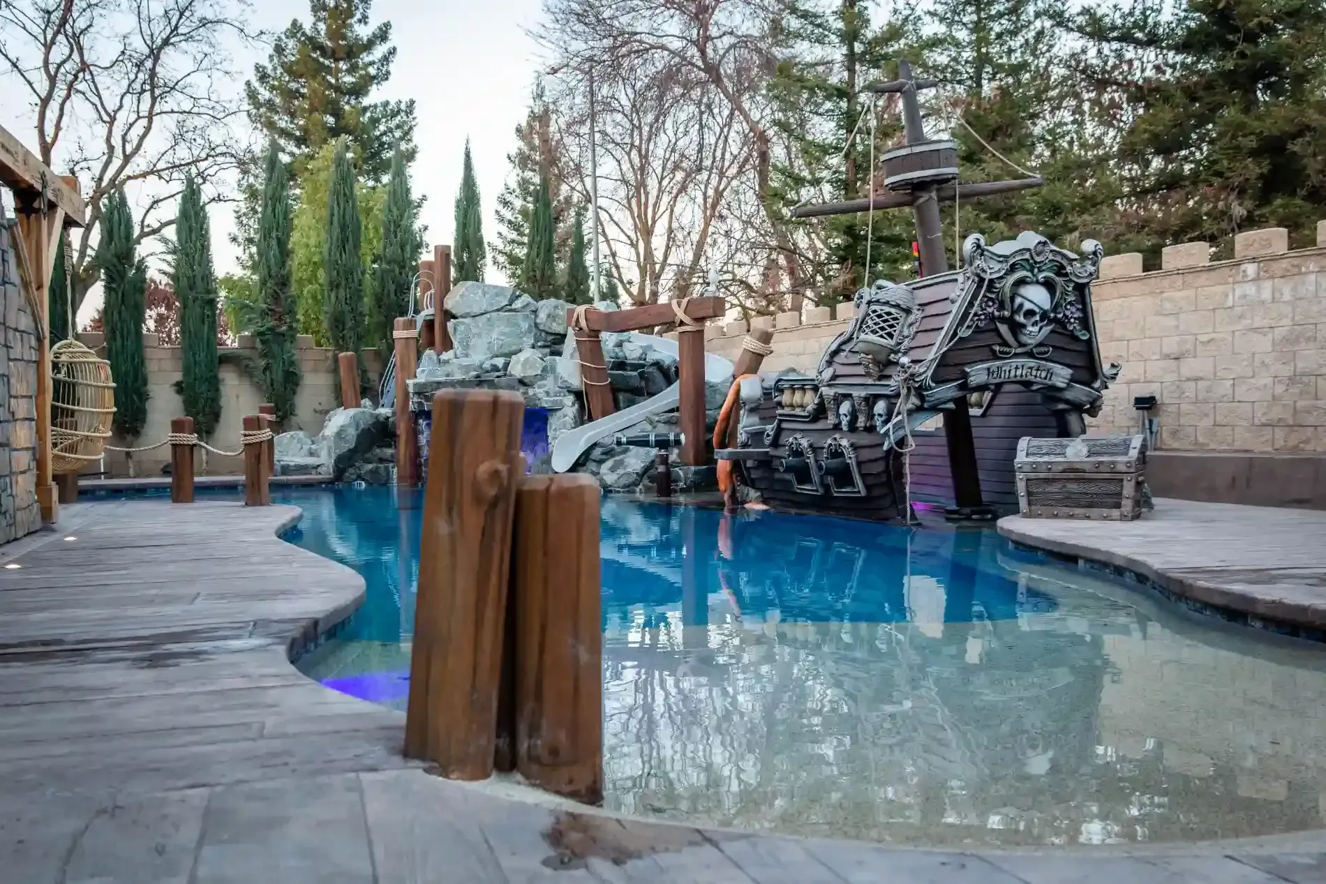 Backyard pool with rock waterfall, stone bridge, and tall trees along the edge