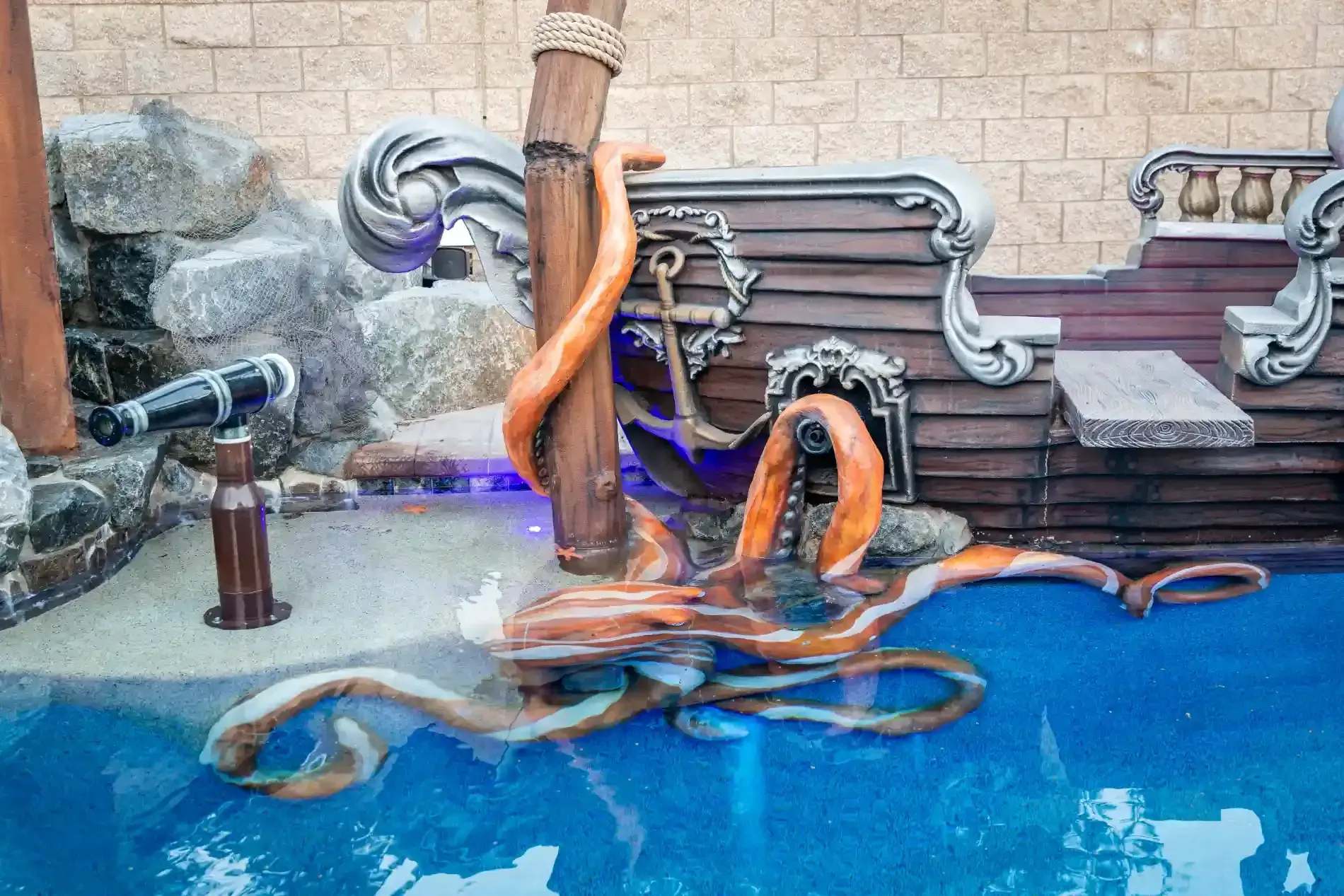 A blue octopus sculpture in a pool beside rocks and a stone wall, with tentacles curling above the water