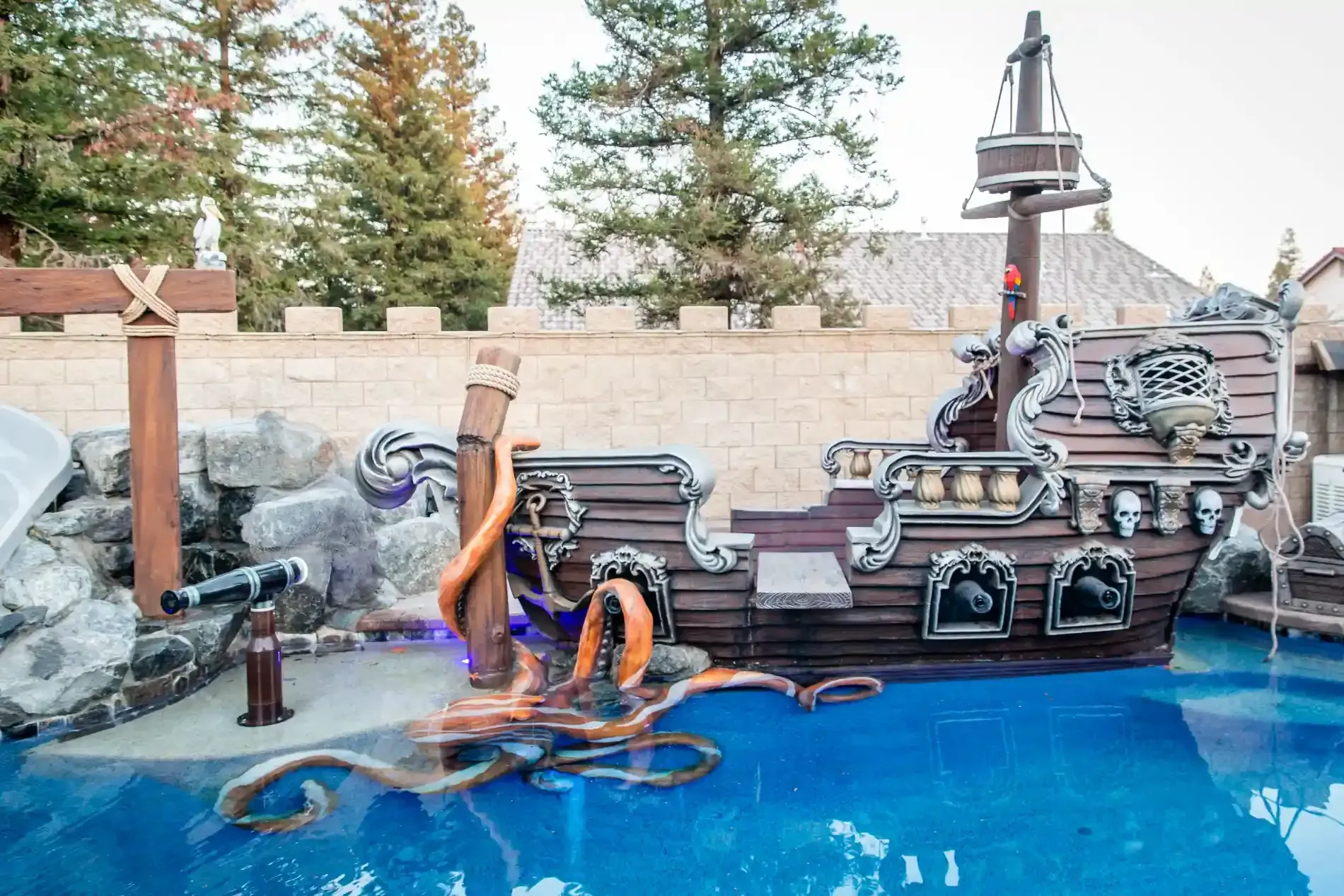 Pirate-themed backyard pool with a ship playset, treasure chest, and orange water slides