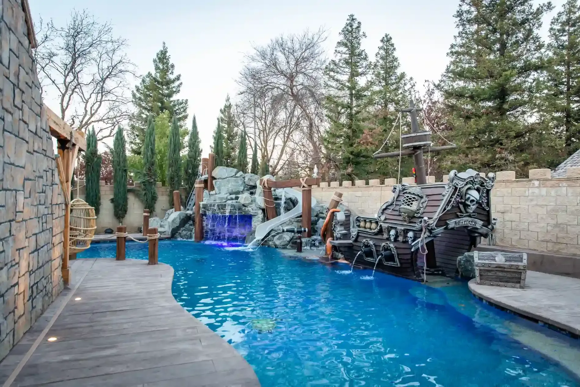 Backyard pool with waterfall rock feature, blue water, and stone patio surrounded by trees