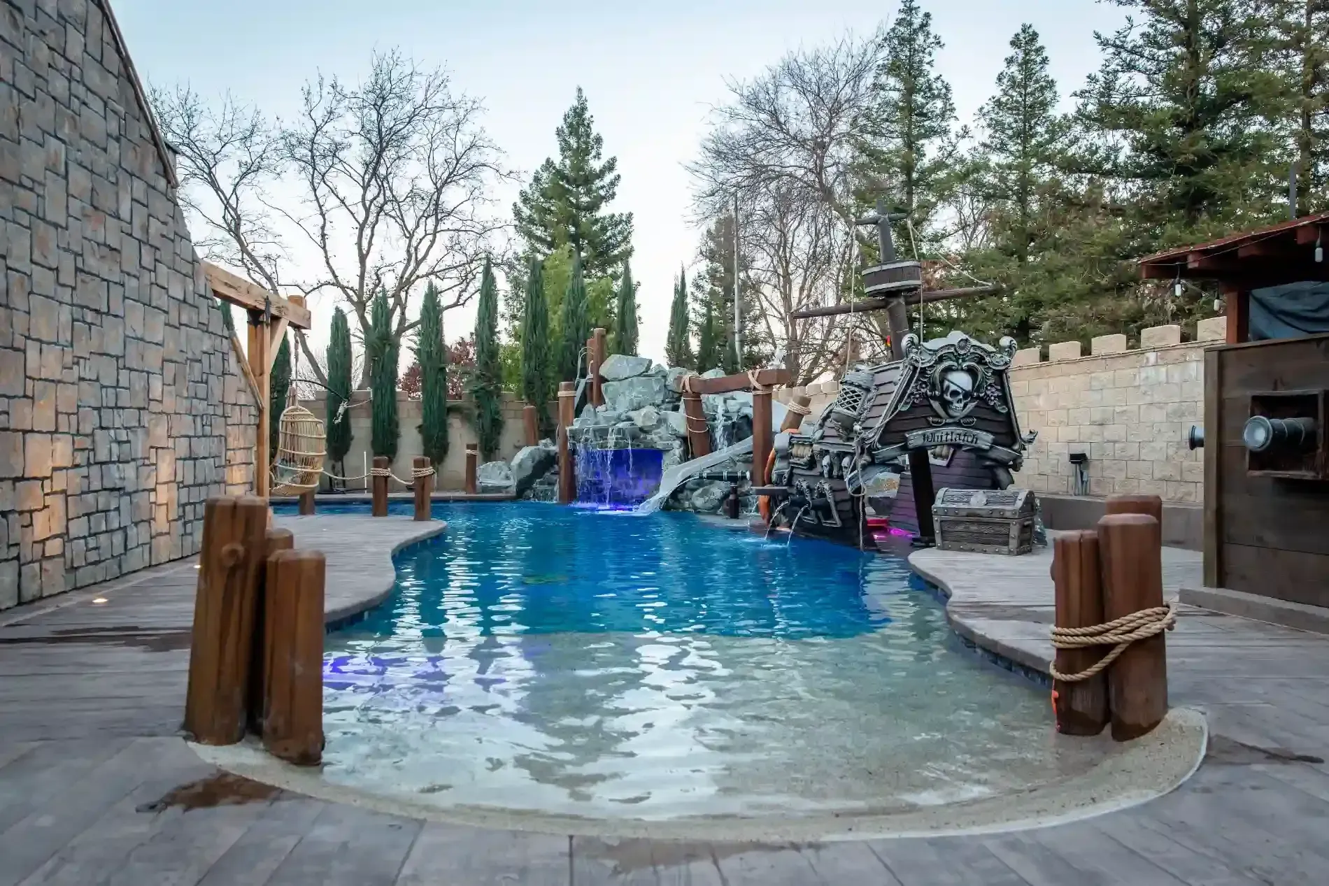 Outdoor pool with stone deck, waterfall, and trees in a landscaped backyard