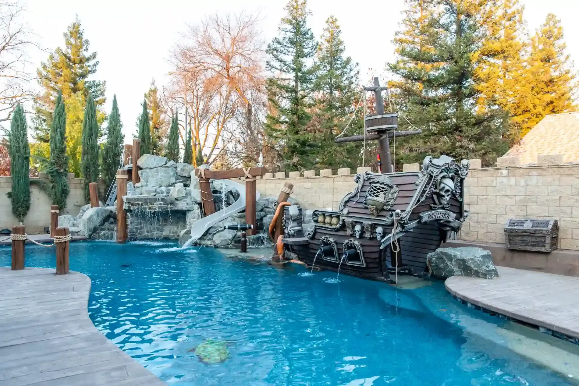 Backyard pool with waterfall rocks and lounge chairs, surrounded by autumn trees