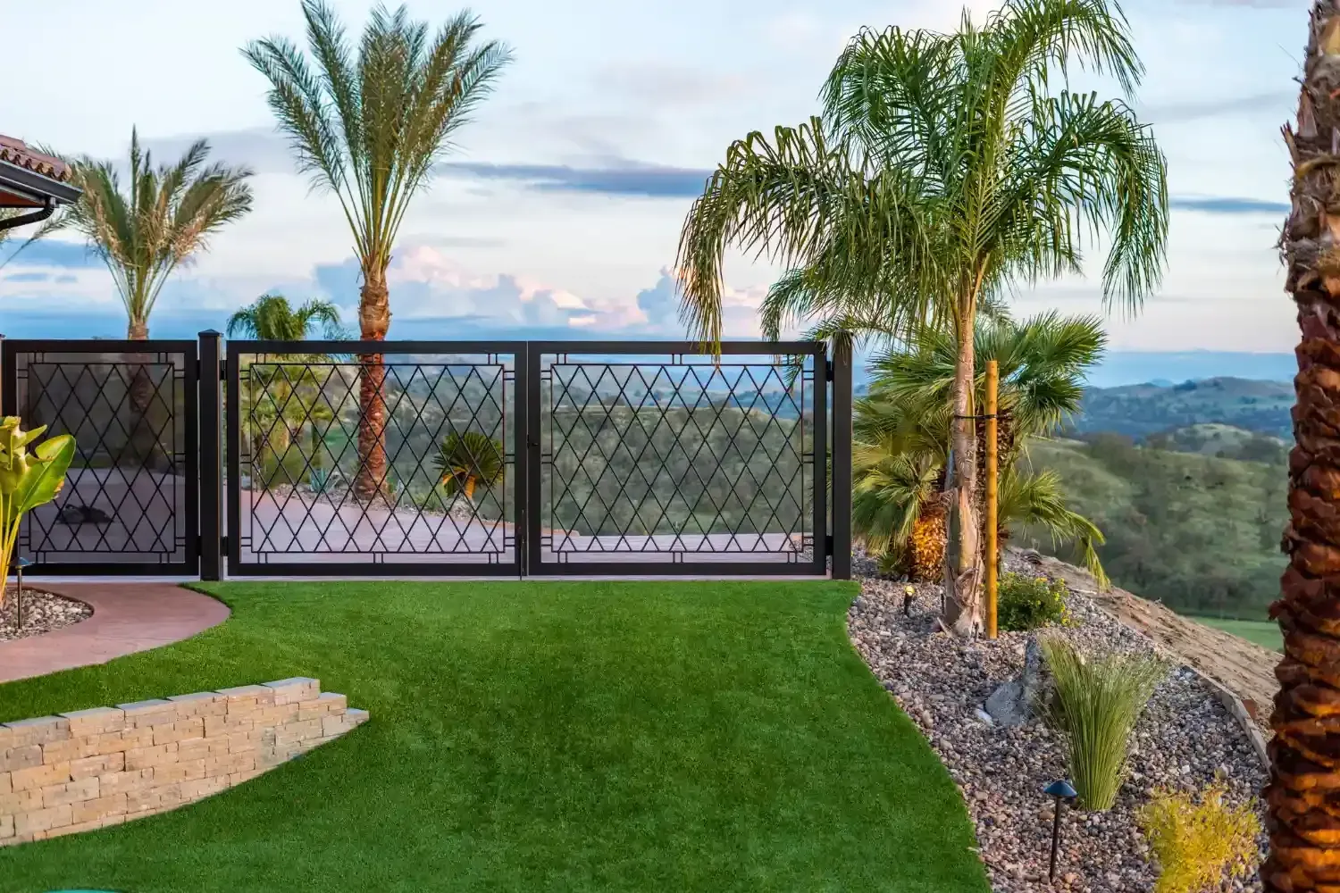 Patio with palm trees, black fence, and sweeping mountain valley view at sunset