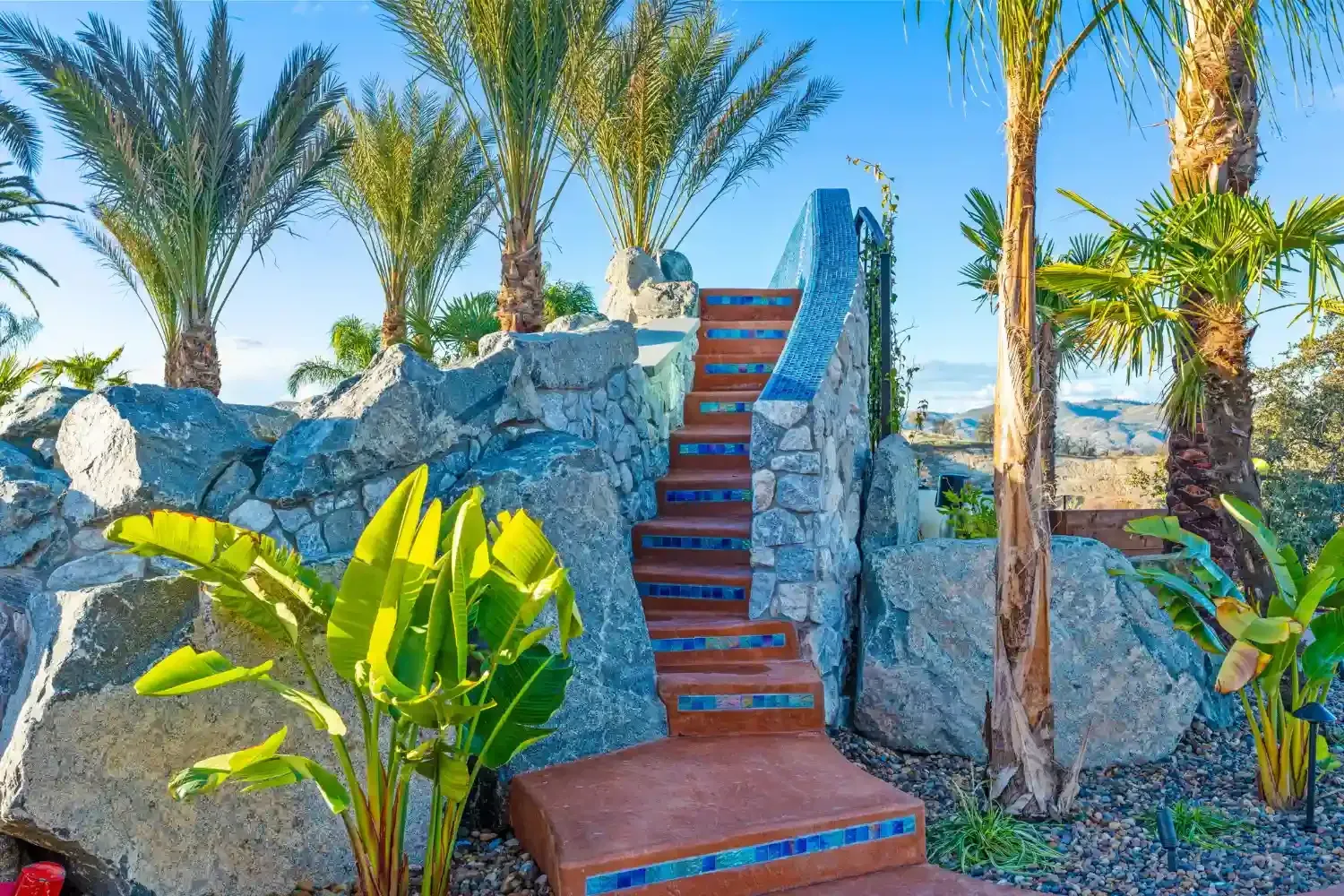 Stairway between large rocks and palm trees in a sunny tropical garden
