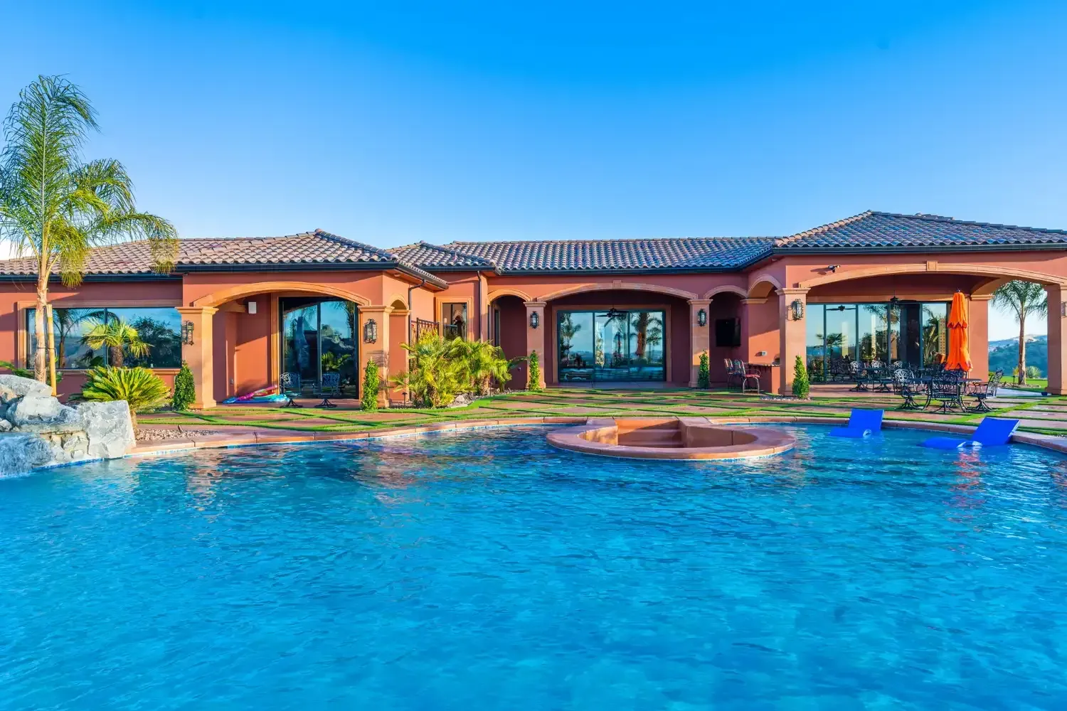 Luxury home with a large blue swimming pool and palm trees under a clear sky
