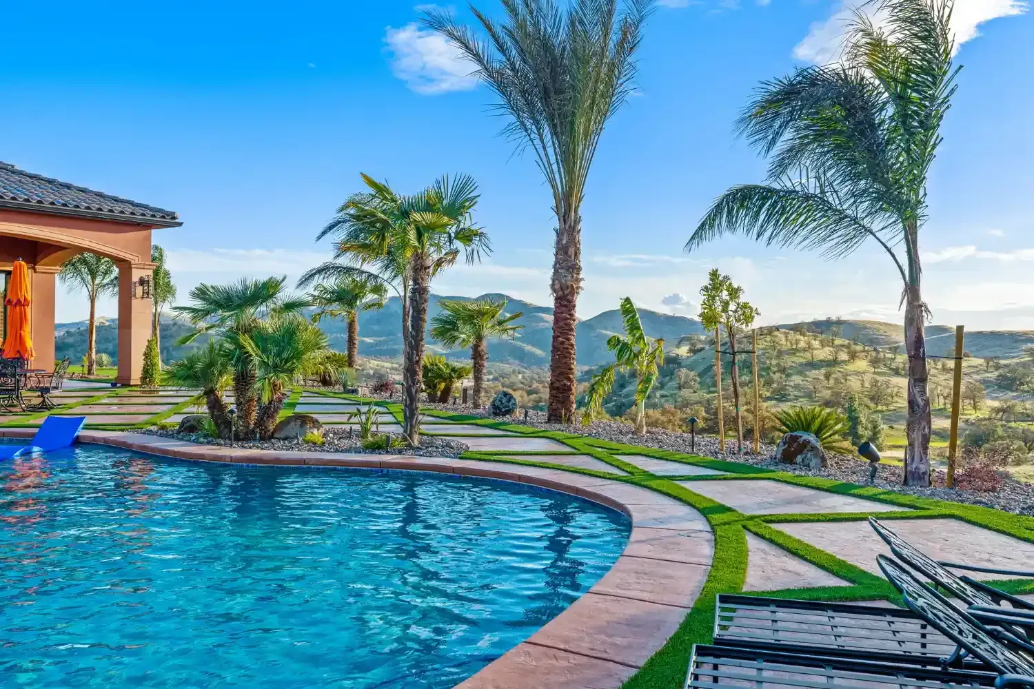 Luxury backyard pool with palm trees, stone patio, and sunset mountain view